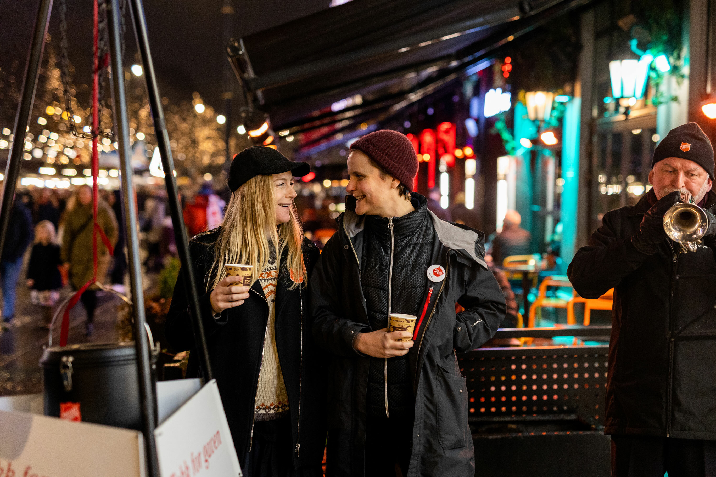Julegryte på Karl Johan. To grytevakter og en uniformert mann som spiller kornett.