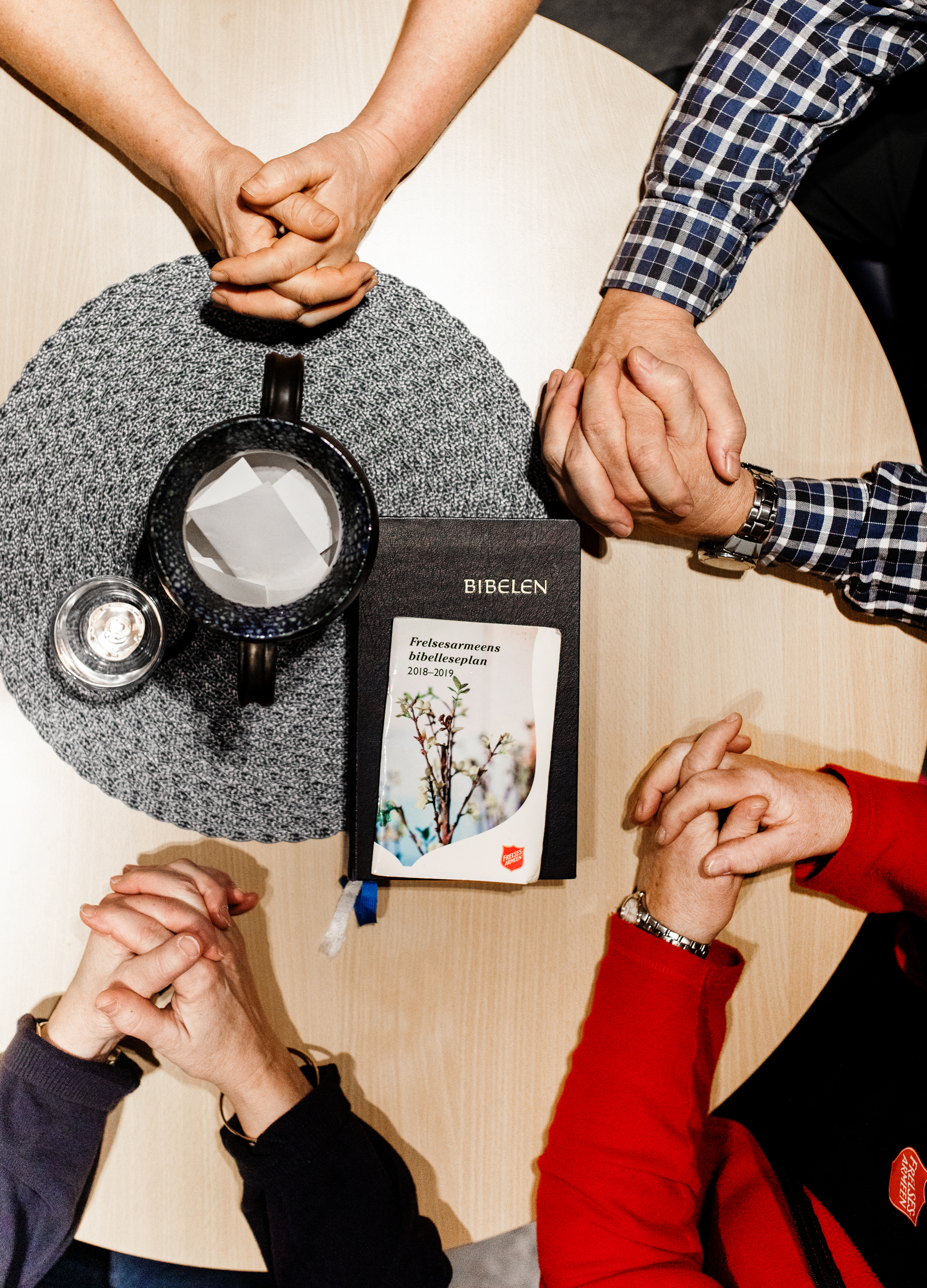 Foldede hender på et bord med lys og bibel -tatt ovenfra