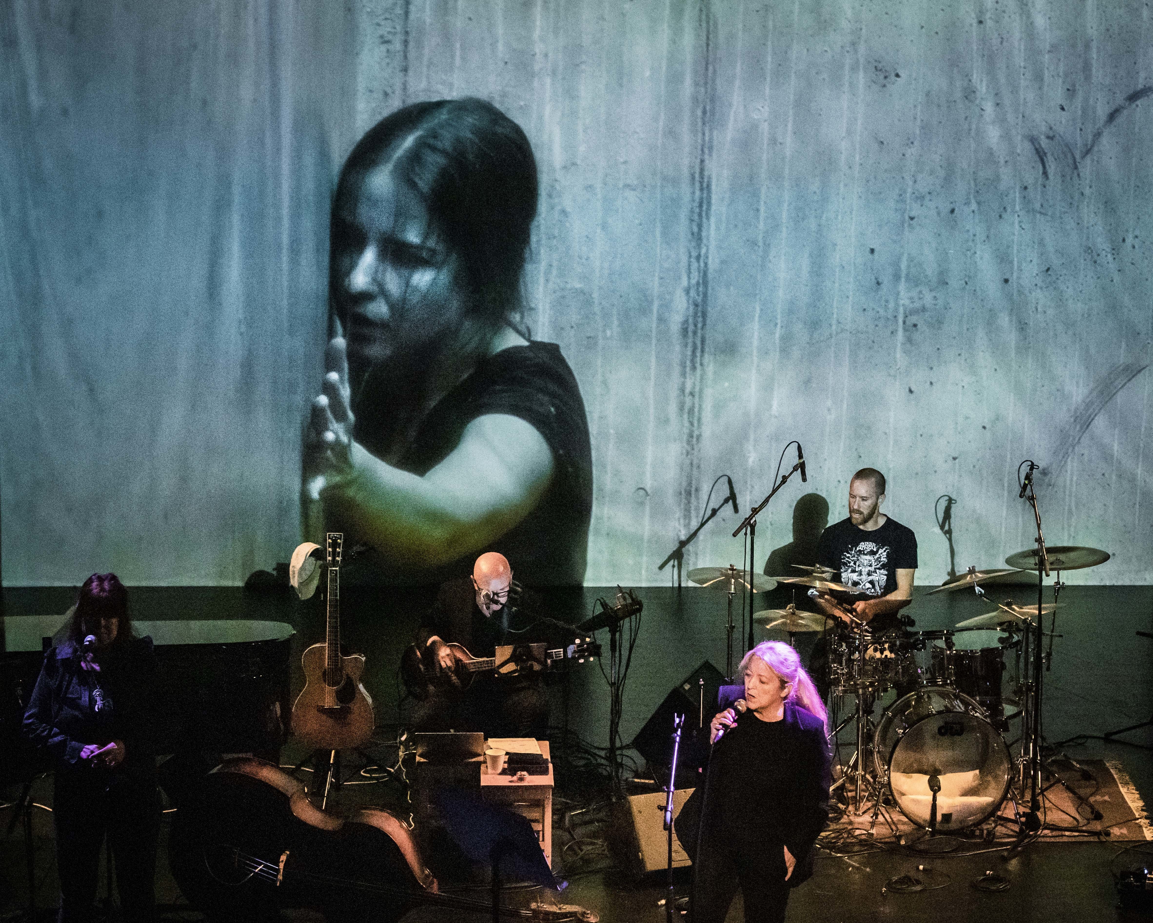 Bilde fra konserten der Lovise AK synger sammen med bandet, med illustrerende bilder på veggen