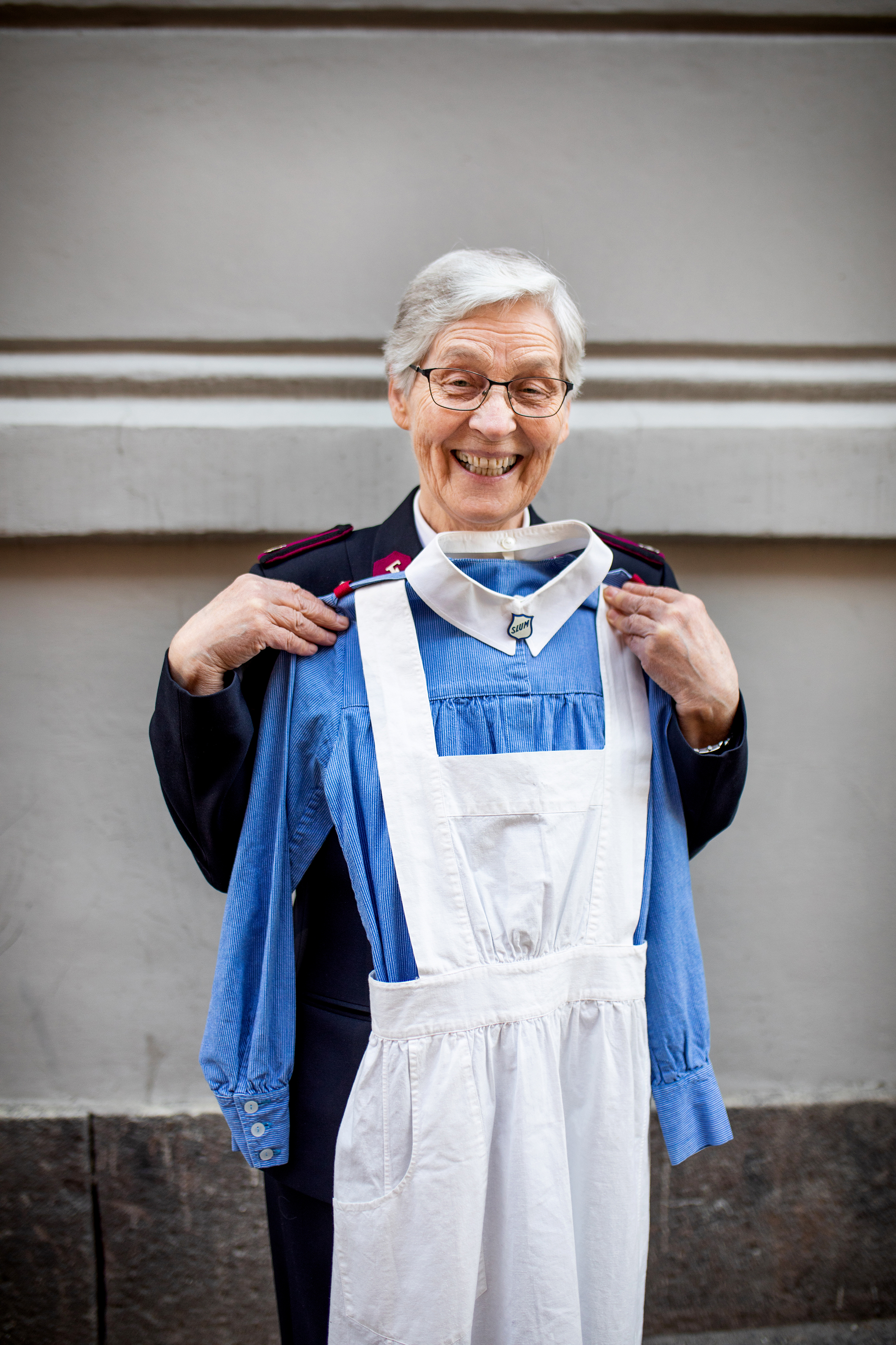Åse Nystuen holder opp en Slumsøster uniform, blå kjole og hvitt forkle.