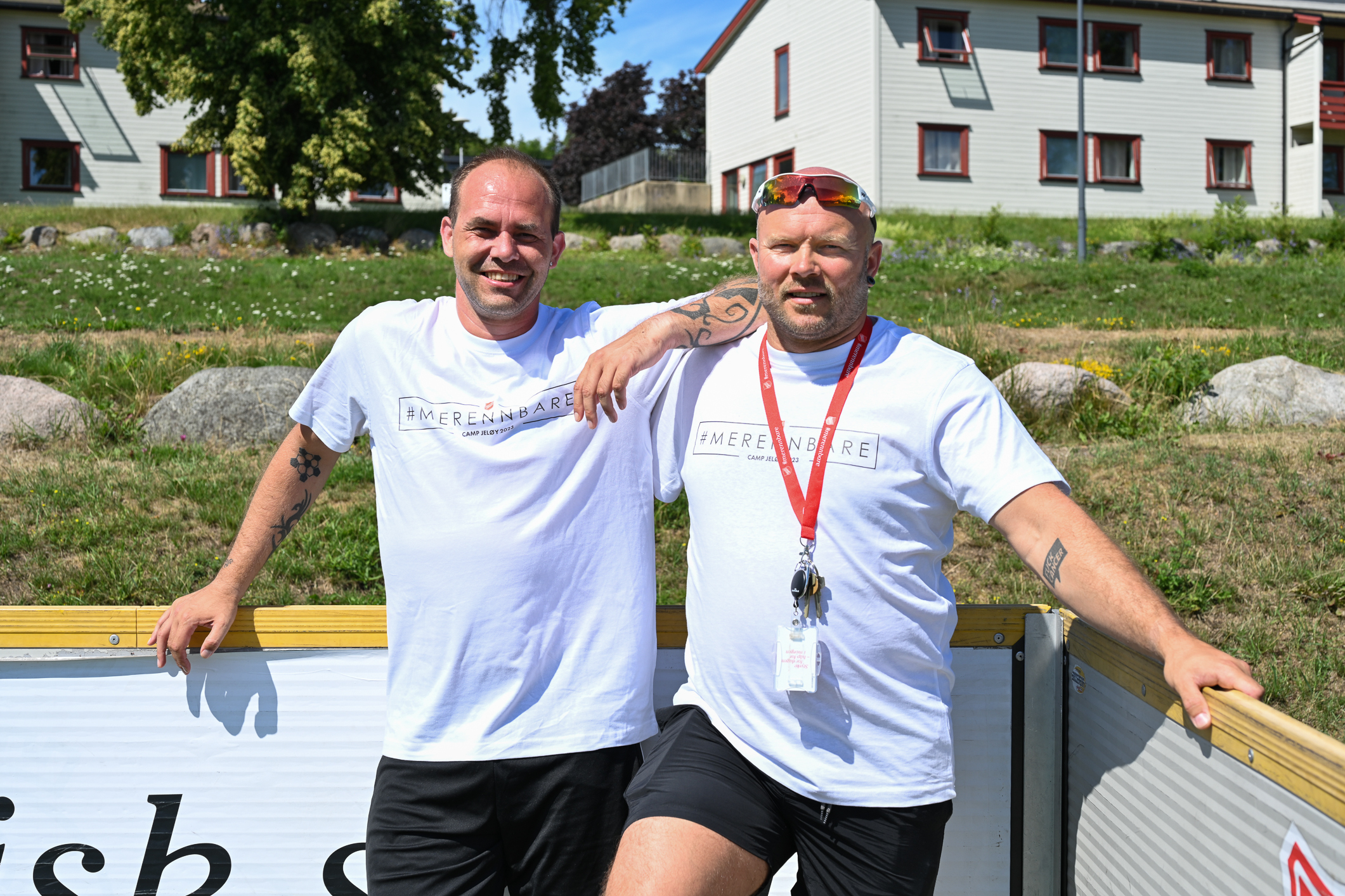 To menn i hvite T-skjorter står tett sammen inni et hjørne av en ballbinge.