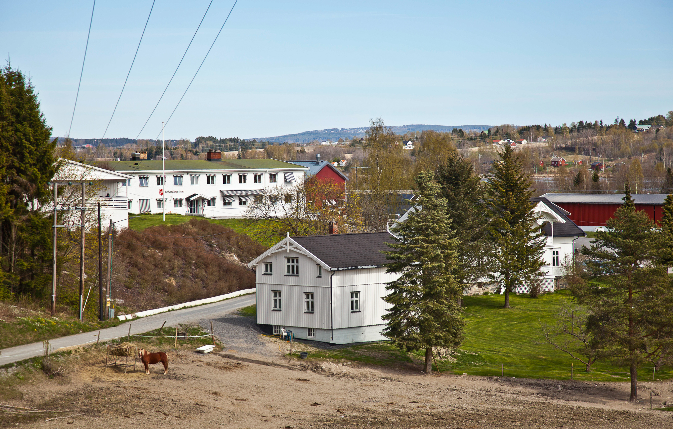 To bilder av samme bygg, der det ene er et bilde tett på og det andre viser skog, et par gårdshus og en hest i forgrunnen.