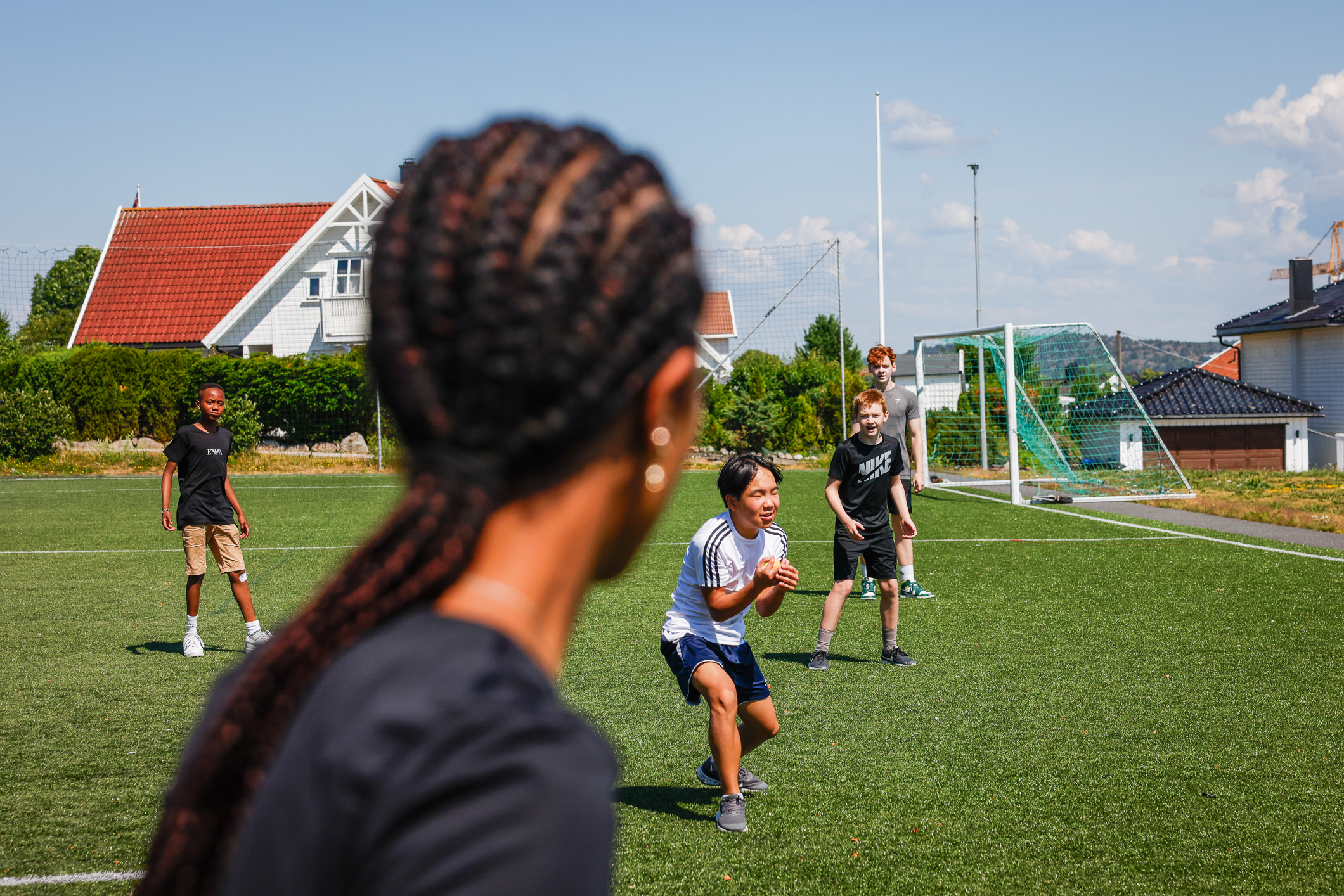 Fire gutter på fotballbanen. En jente står med bakhodet tett inntil kamera. Hun har lange rastafletter.