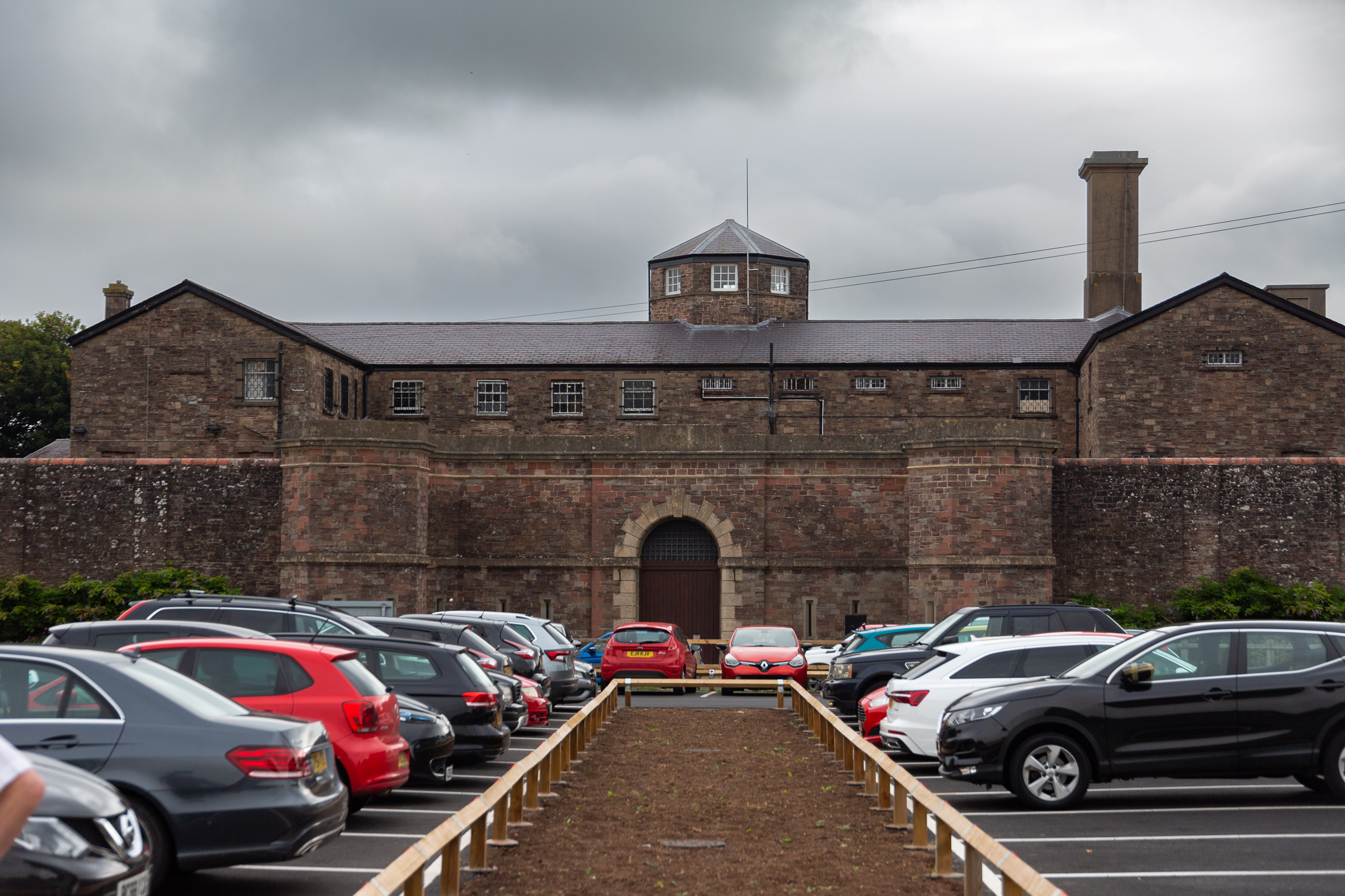 Fengselsbygningen sett utenfra - en stor murbygning med høye porter og et annet blått bygg med skog rundt.