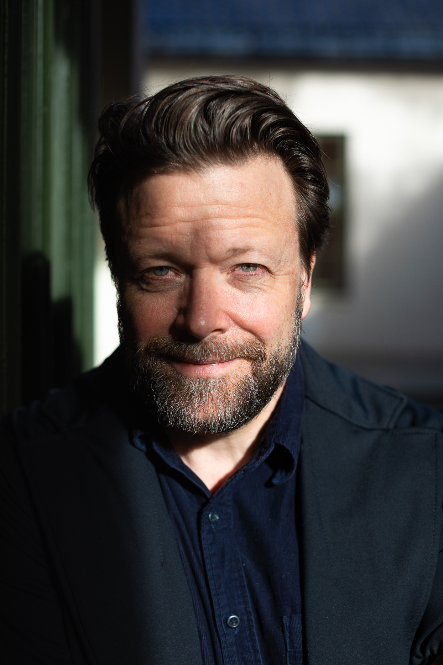 Alvorlig mann i 50-årene med skjegg og mye hår på hodet ser inn i kamera. Bildet er tett på hodet hans. Over ansiktet er det delvis litt skygge.