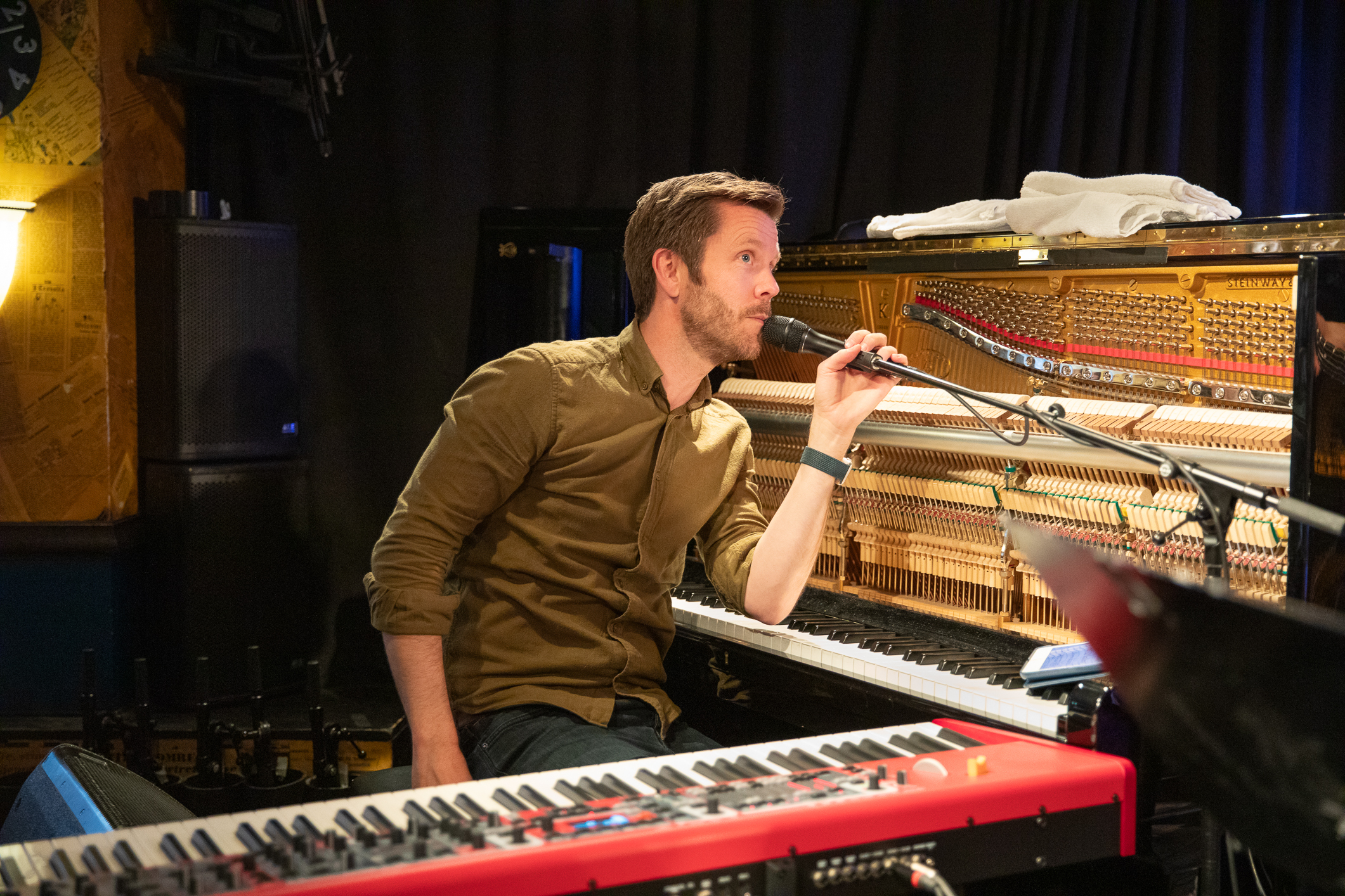 Mann som sitter ved et piano. Han synger i mikrofonen.