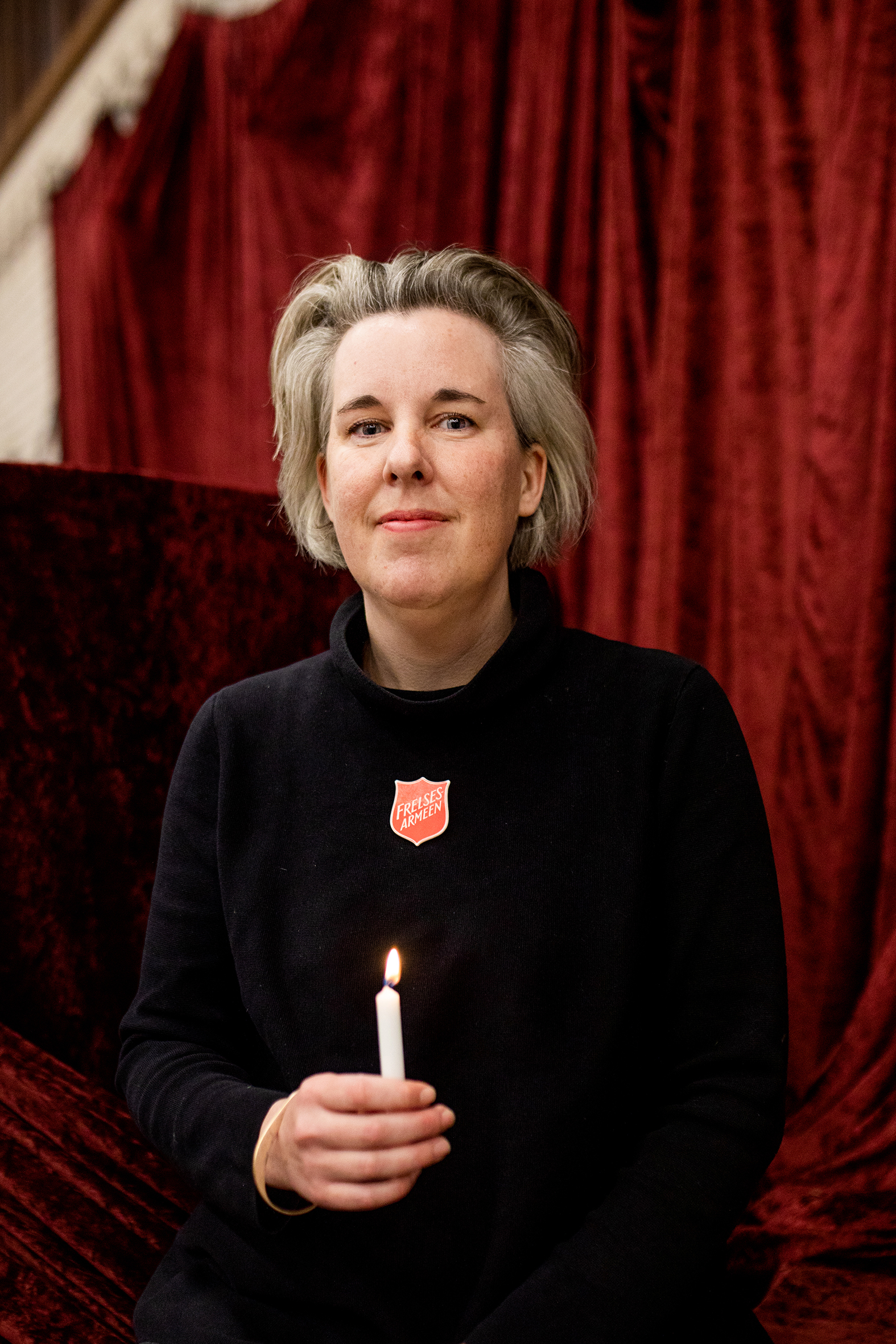 Bildet viser Kjellgren som står foran et mørkerødt forheng. Hun holder et tent, hvitt stearinlys.