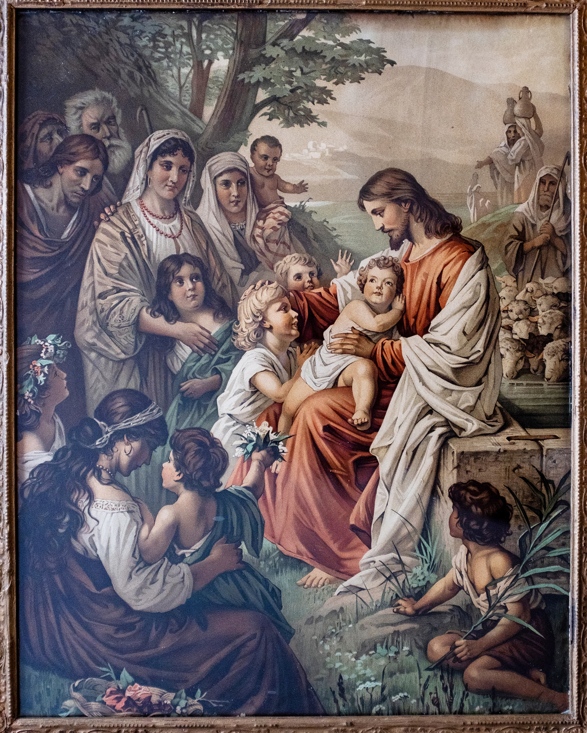 Bildet er et gammelt maleri av Jesus og barna. Han har et barn på fanget og mange barn rundt seg, mens flere voksne står litt lenger unna.
