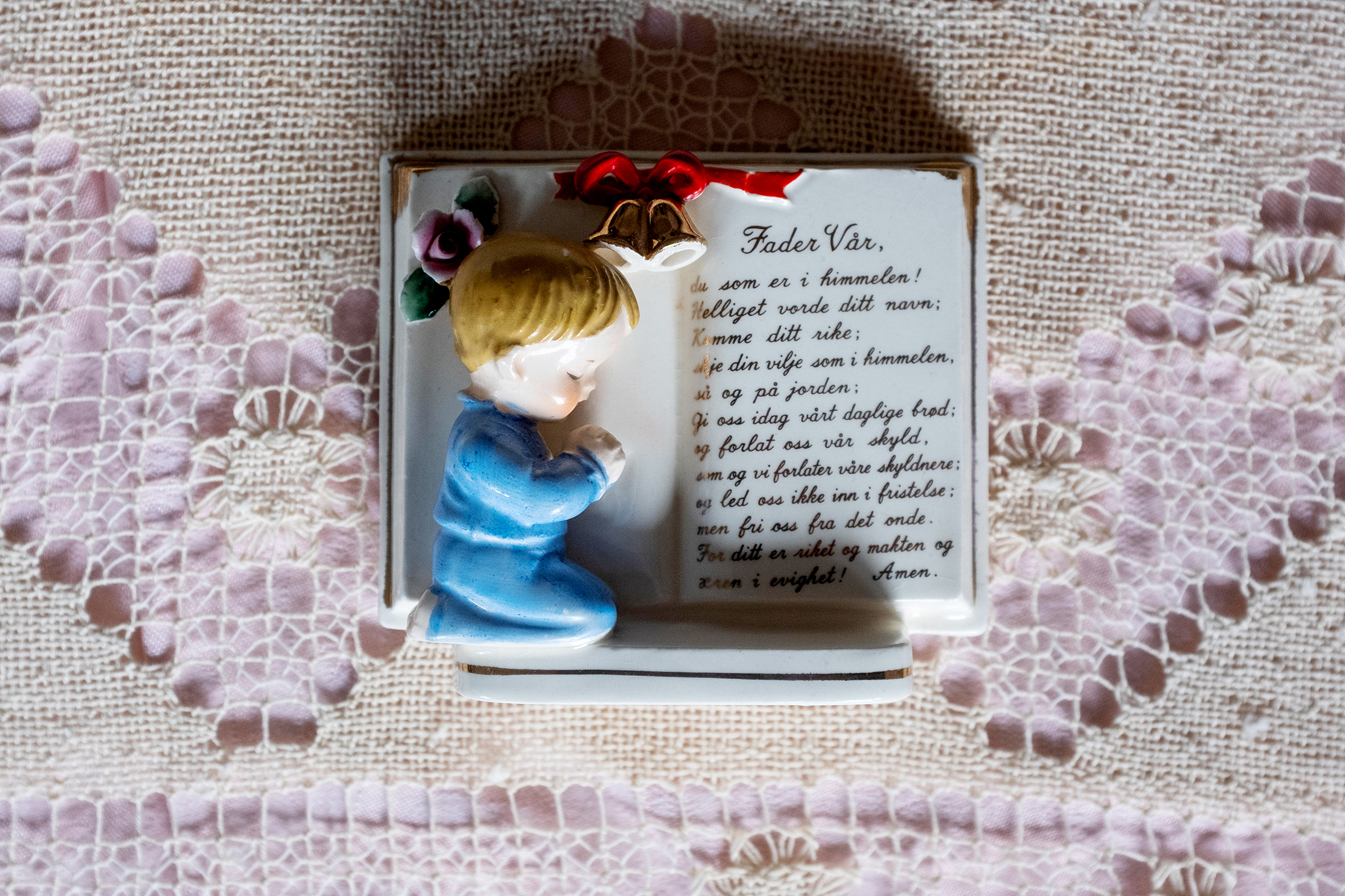Bildet viser en gammel porselensfigur formet som en bok, med en liten gutt med foldede hender og bønnen Fader vår.