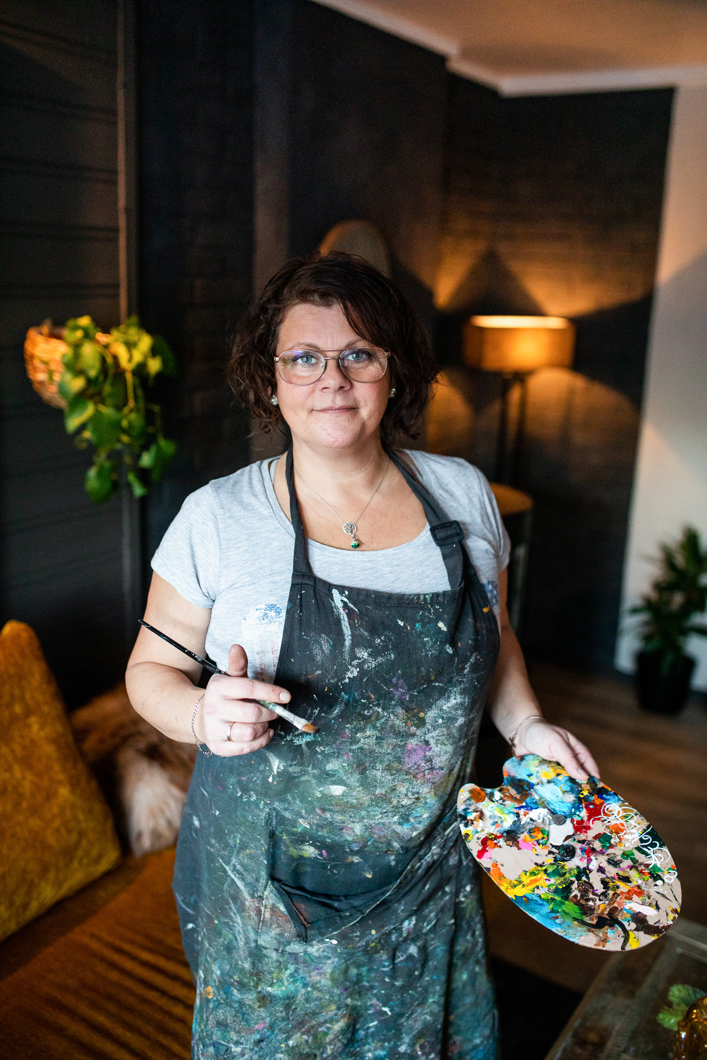 Aina i et forkle full av malingsflekker, og pensel i hånden