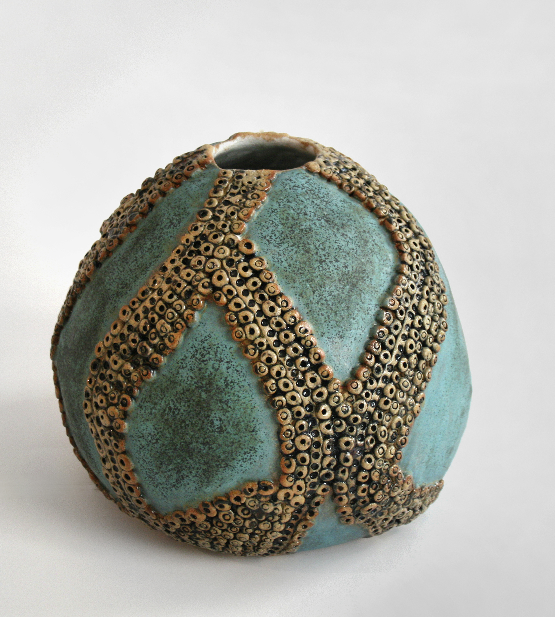 Bildet viser et kunstverk i keramikk. Det er en blågrønn krukke, med mange små sirkler som utgjør et mønster.