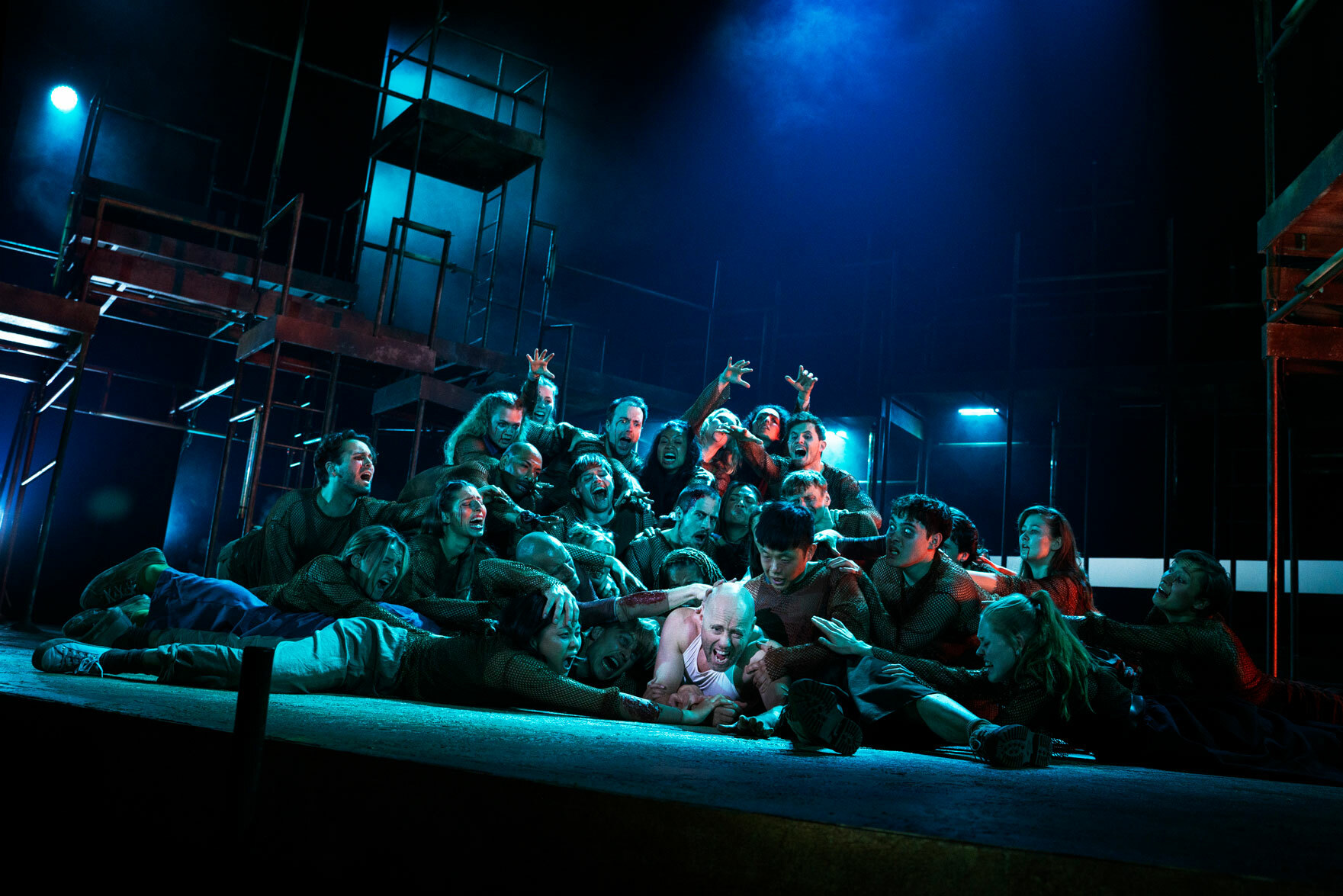 Foto: Fra en scene, der en skallet mann i hvit trøye ligger nederst på gulvet. Over ham ligger den mange, menge mennesker i en haug.