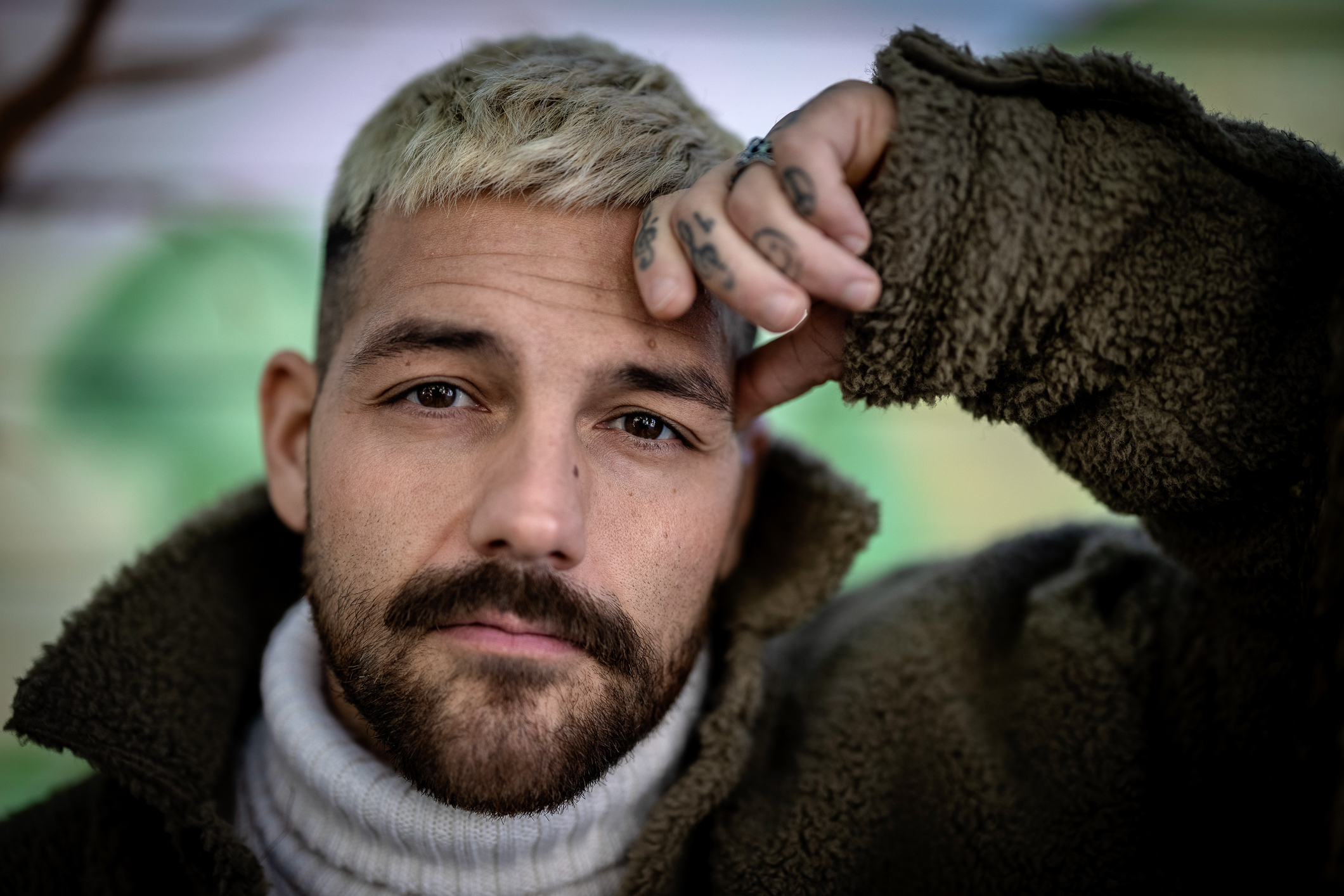 To foto etter hverandre, der det første er et nærbilde av mann med bleket hår og mørkt skjegg og øyne. Han holder en tatovert hånd opp mot venstre side av pannen. Det neste bildet viser begge de tatoverte hendene.