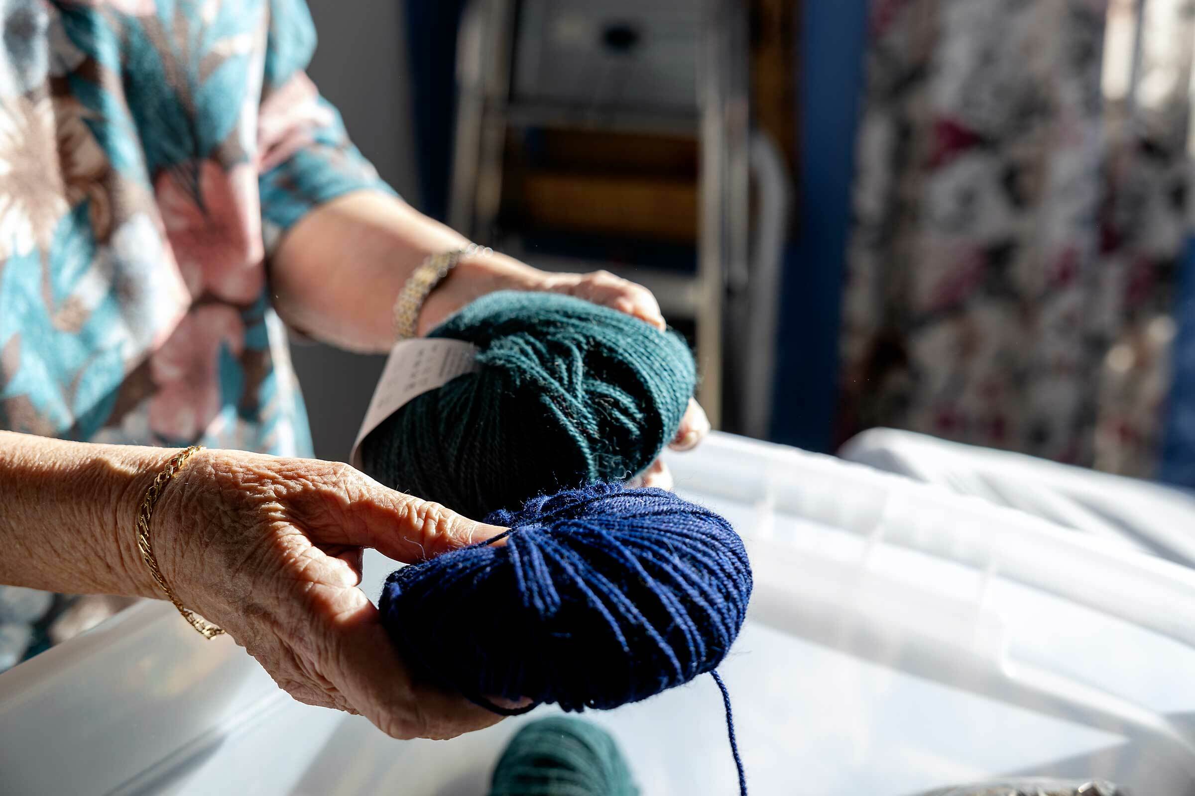 Hender holder to nøster med garn i blått og sjøgrønt.