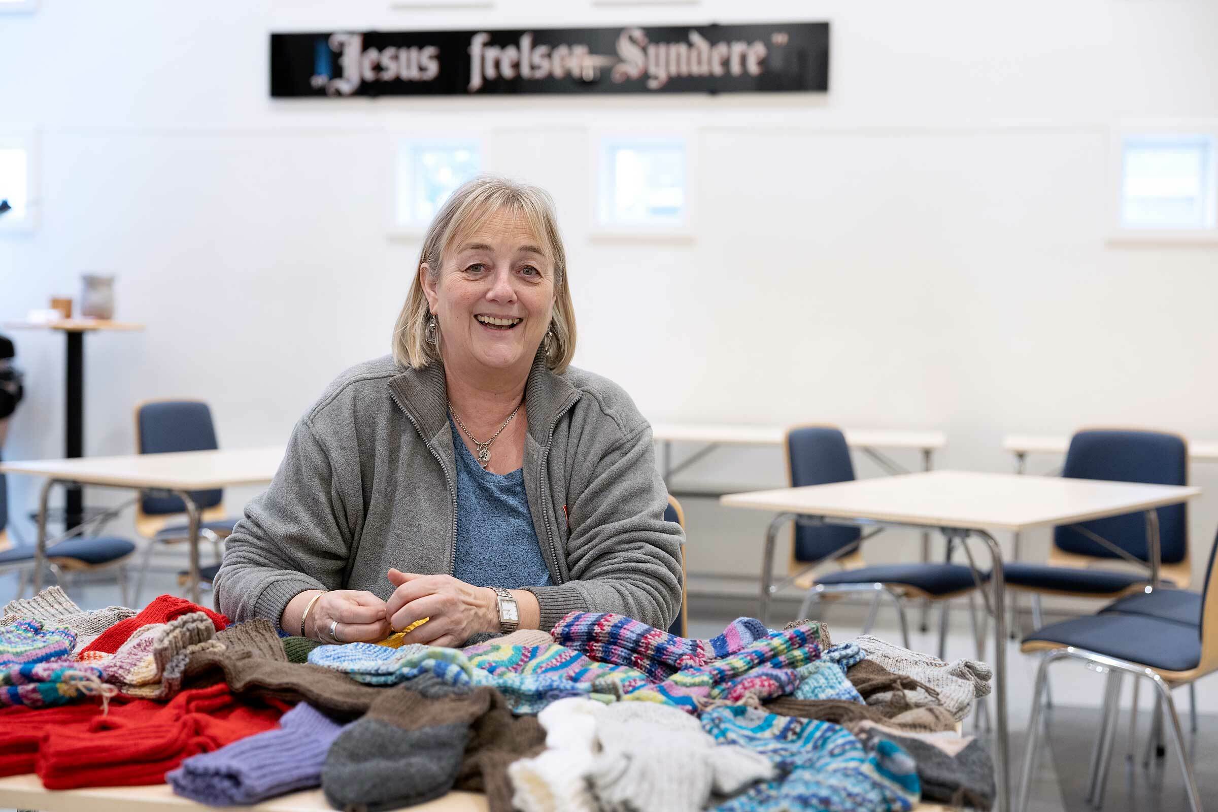Middelaldrende kvinne med halvlangt hår sitter bak et bord fullt av stikkede sokker.