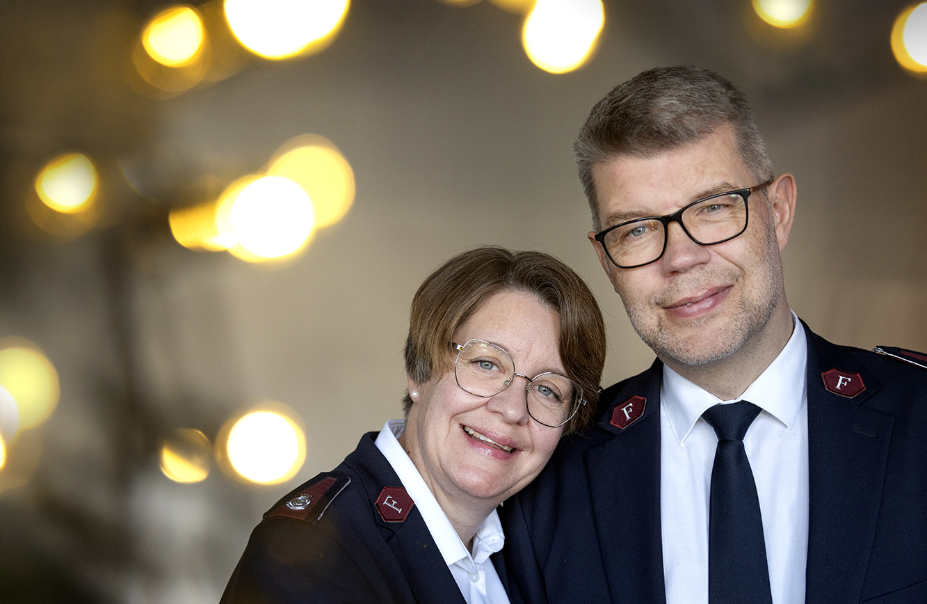 Foto: Kvinne og mann i 50-årene lener seg mot hverandre. I bakgrunnen er det mange lys. Begge bruker briller og har på seg uniforma fra Frelsesarmeen.