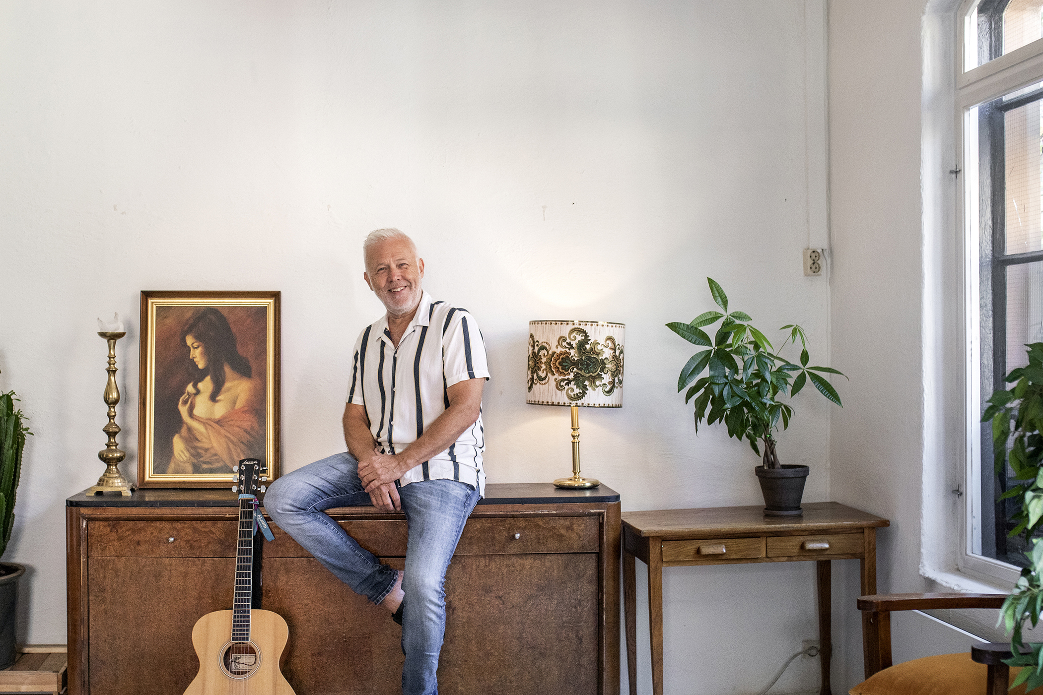 Amund Enger sitter på en kommode. Gitaren står ved siden av.