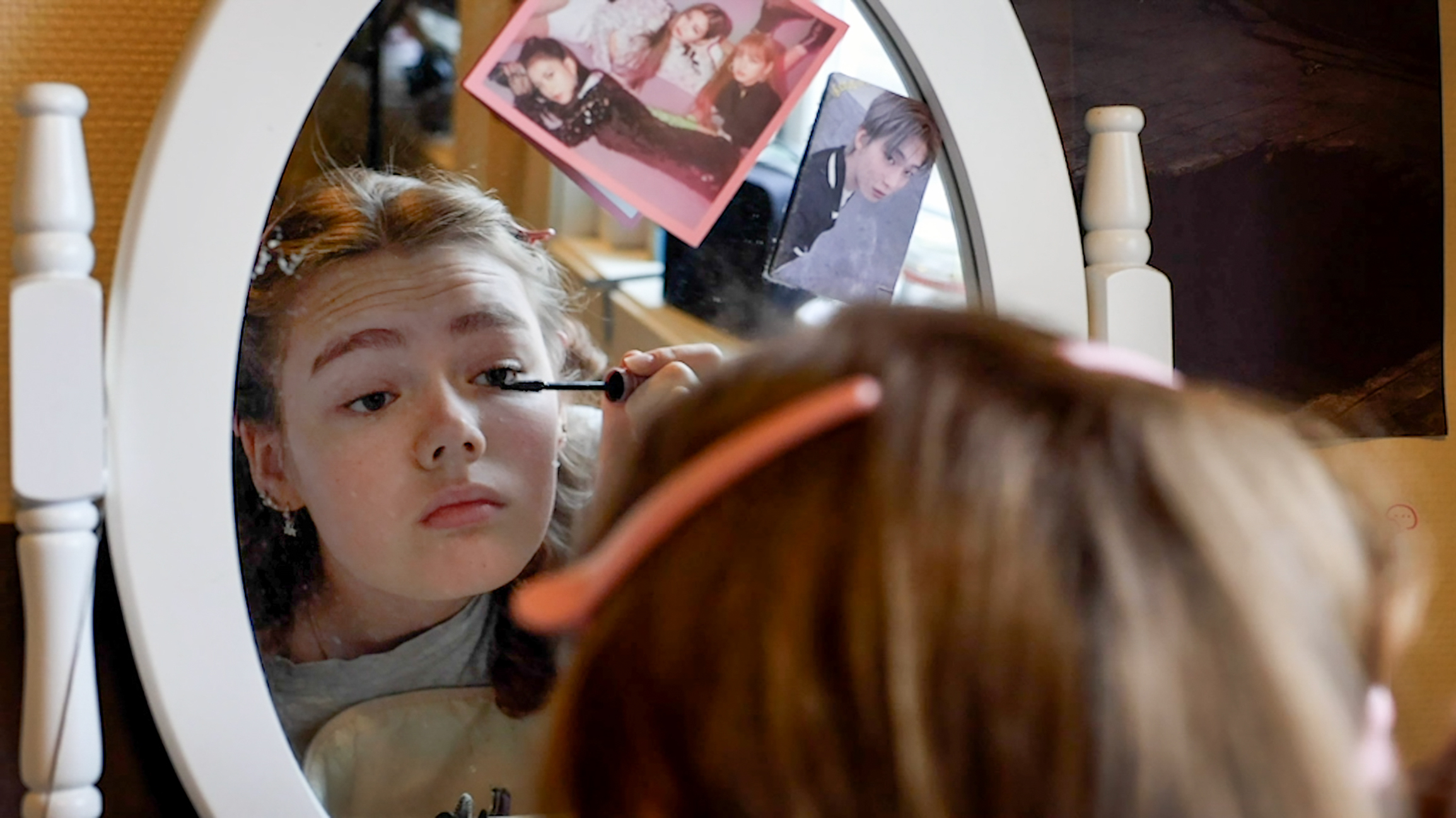 Tenåringsjente som sitter og sminker seg foran speilet.