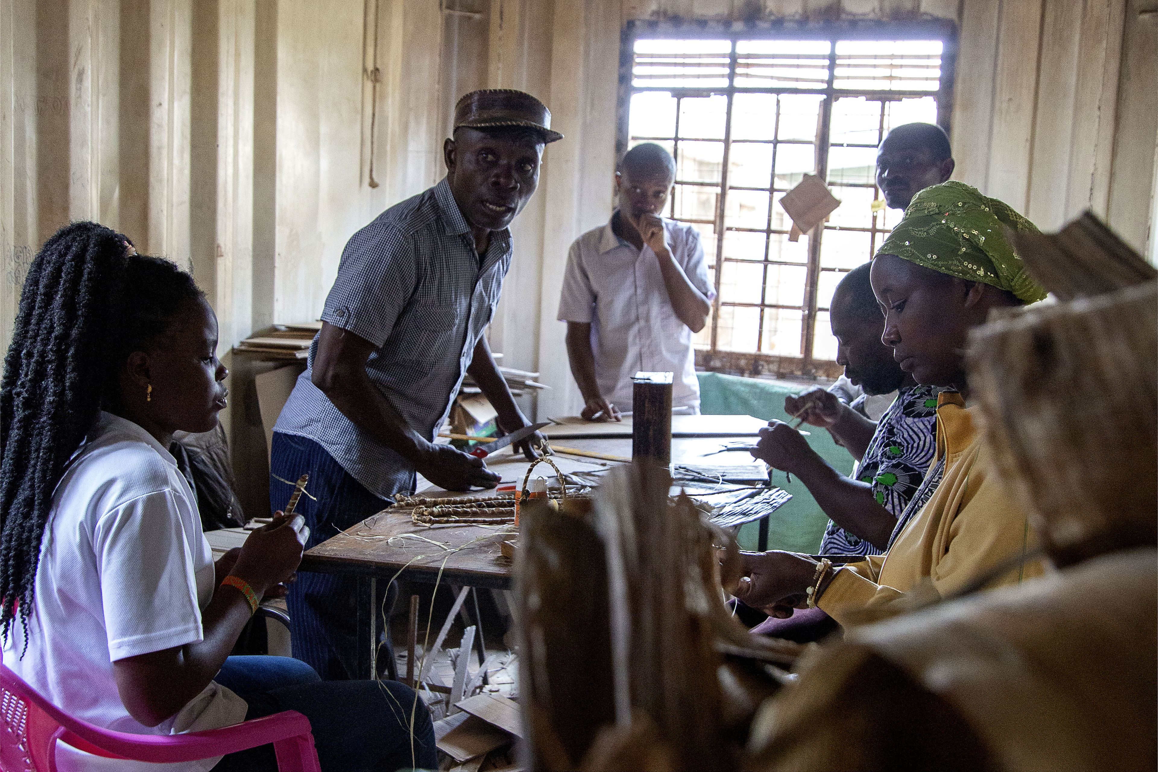 Afrikanske kvinner og menn sitter ved et bord inne i et skur. De produserer deler til håndlagde julekrybber.