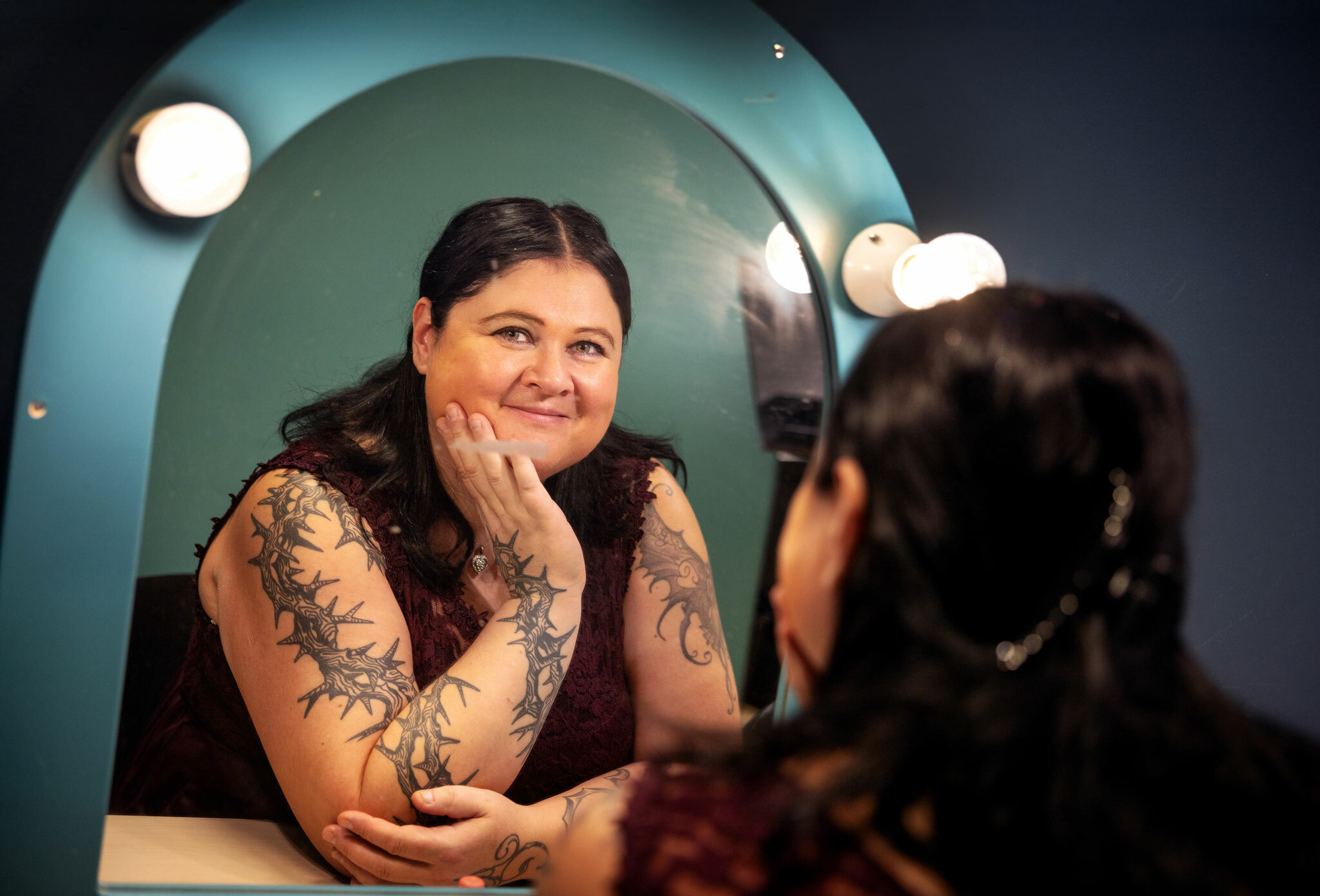 Foto: Kvinne som ser på seg selv i speilet. Hun har kjole uten ermer og har mange tatoveringer oppover.