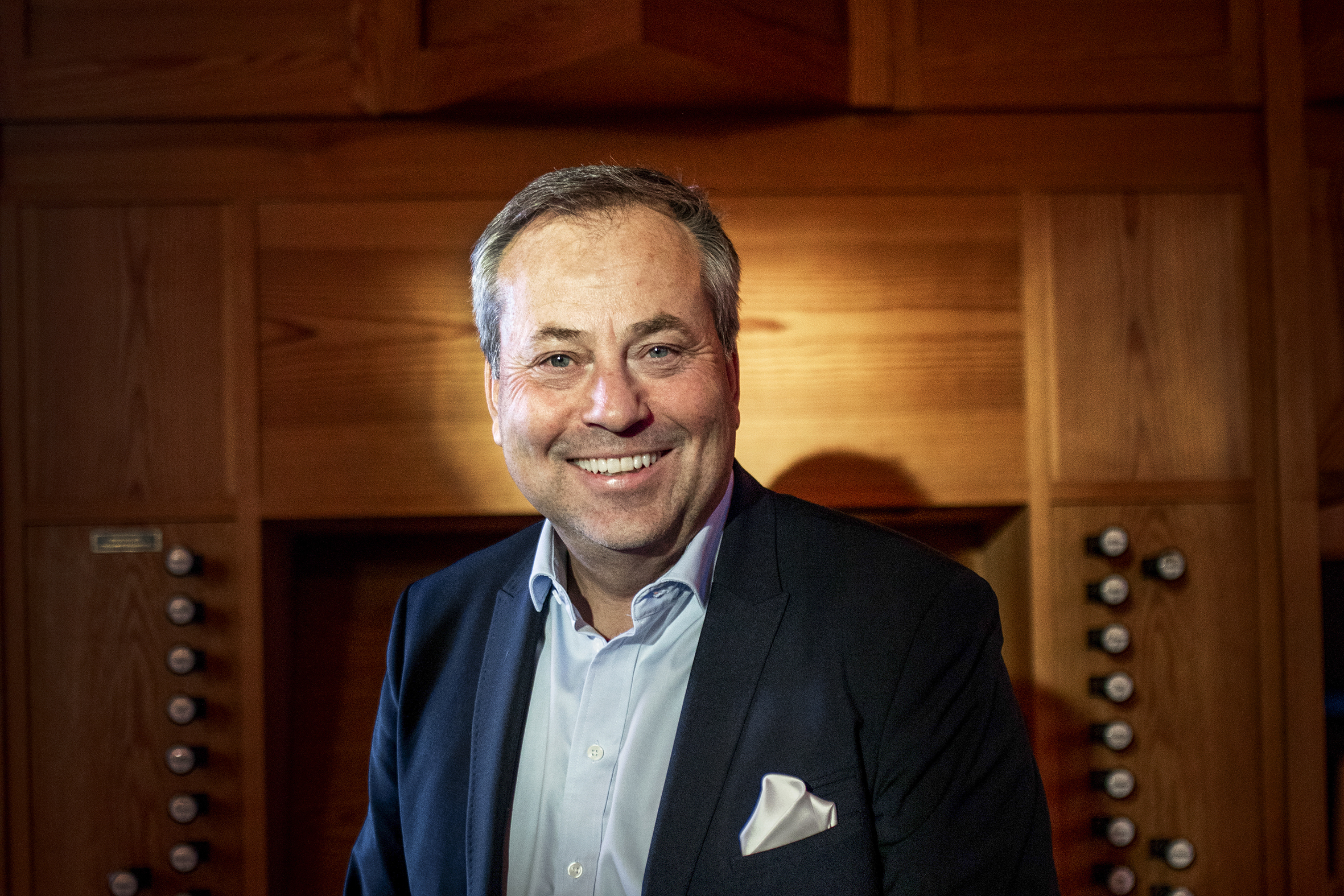 Arve Juritzen sitter smilende på organistbenken i Skøyen kirke. Sollyset kom inn gjennom vinduet og lyser opp ansiktet hans.