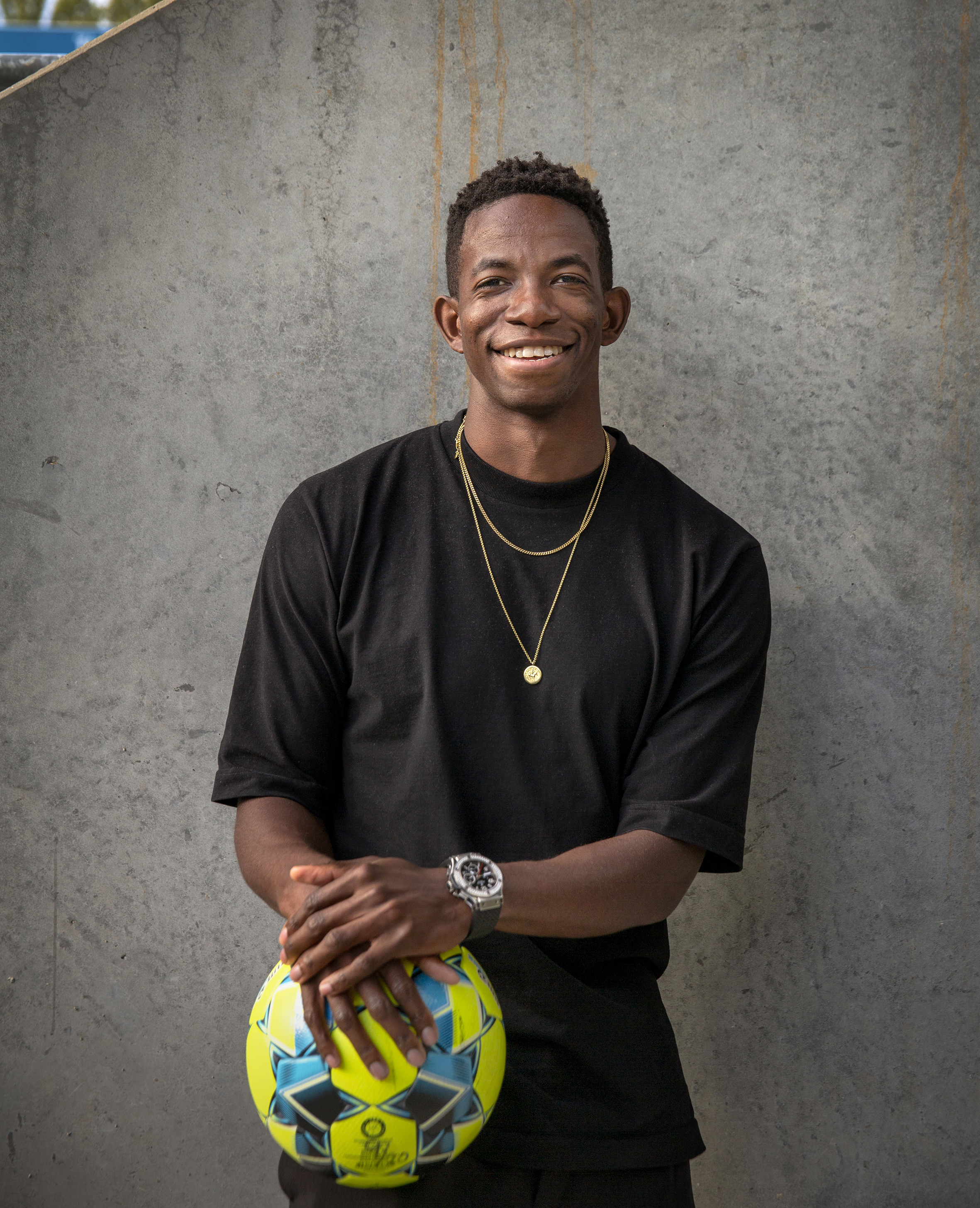 Bildet viser Bakenga som står foran en murvegg og holder en fotball.