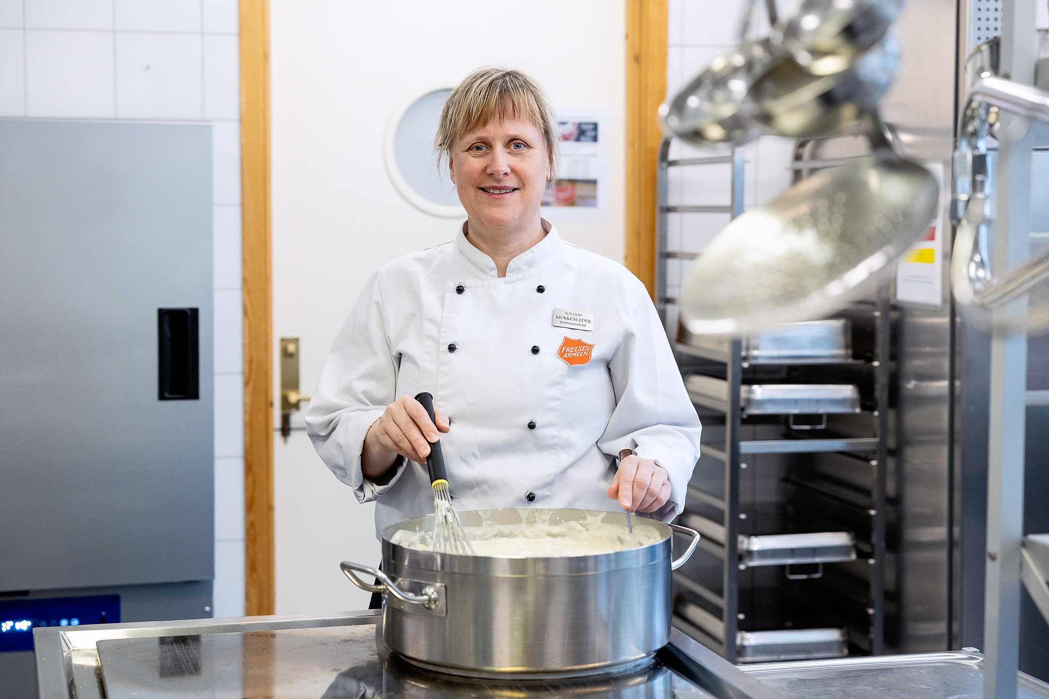 Kvinne i hvit kokkeuniform rører i en diger gryte.