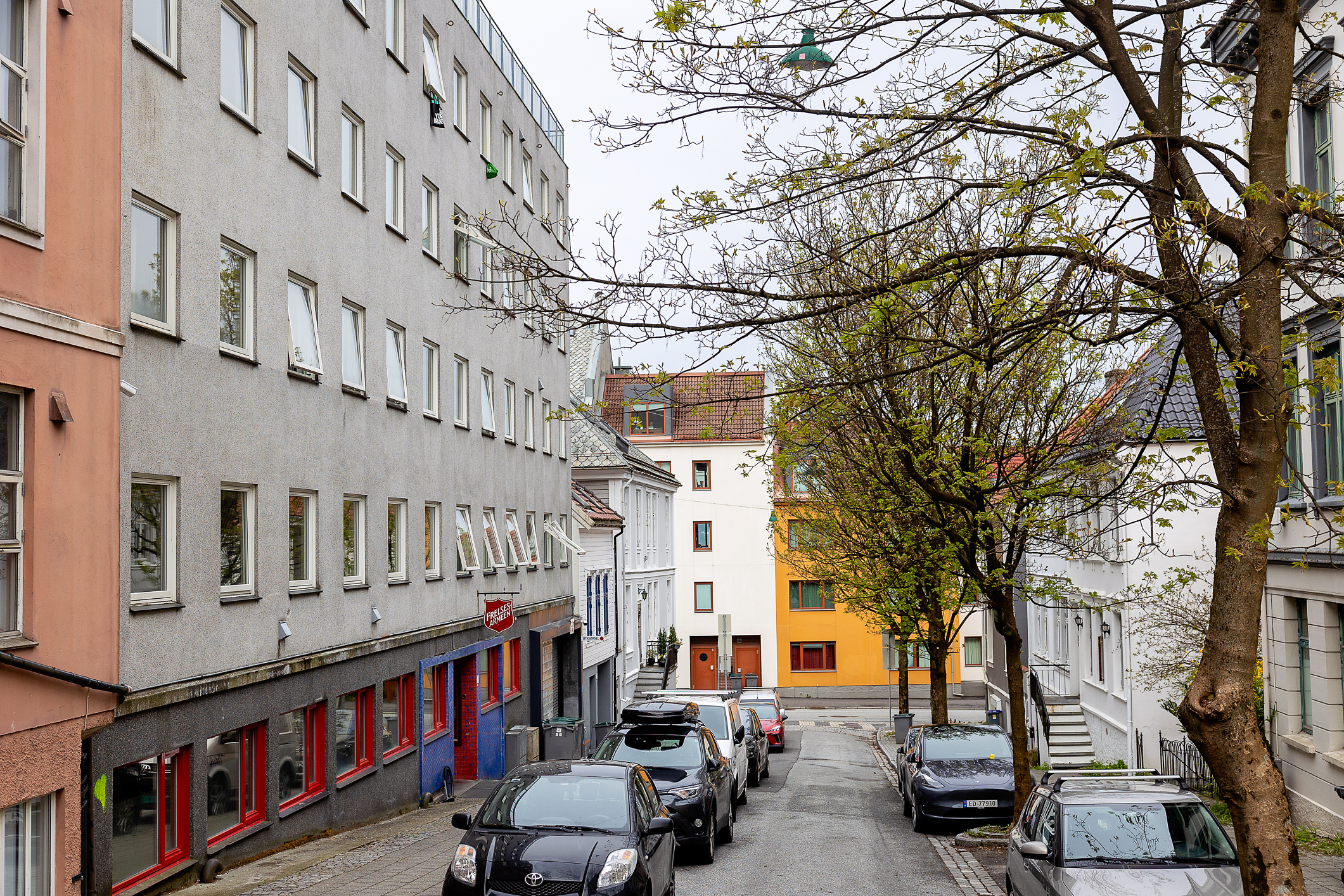 Bilde av en bygate som ligger i en bakke. På venstre side av et grått bygg henger et skilt til Frelsesarmeen.