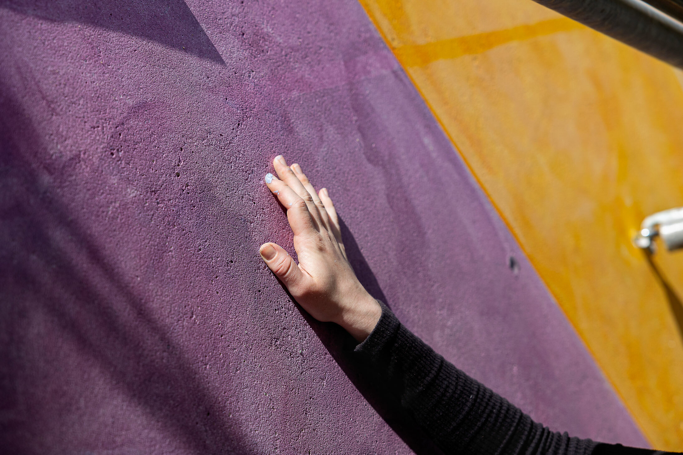 Foto: En hånd ligger klapper på en malt murvegg.