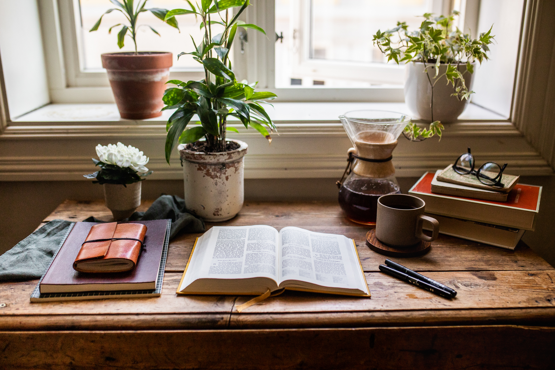 Oppslått bibel på skrivebord ved vinduet. Kaffekopp og planter i bakgrunnen.