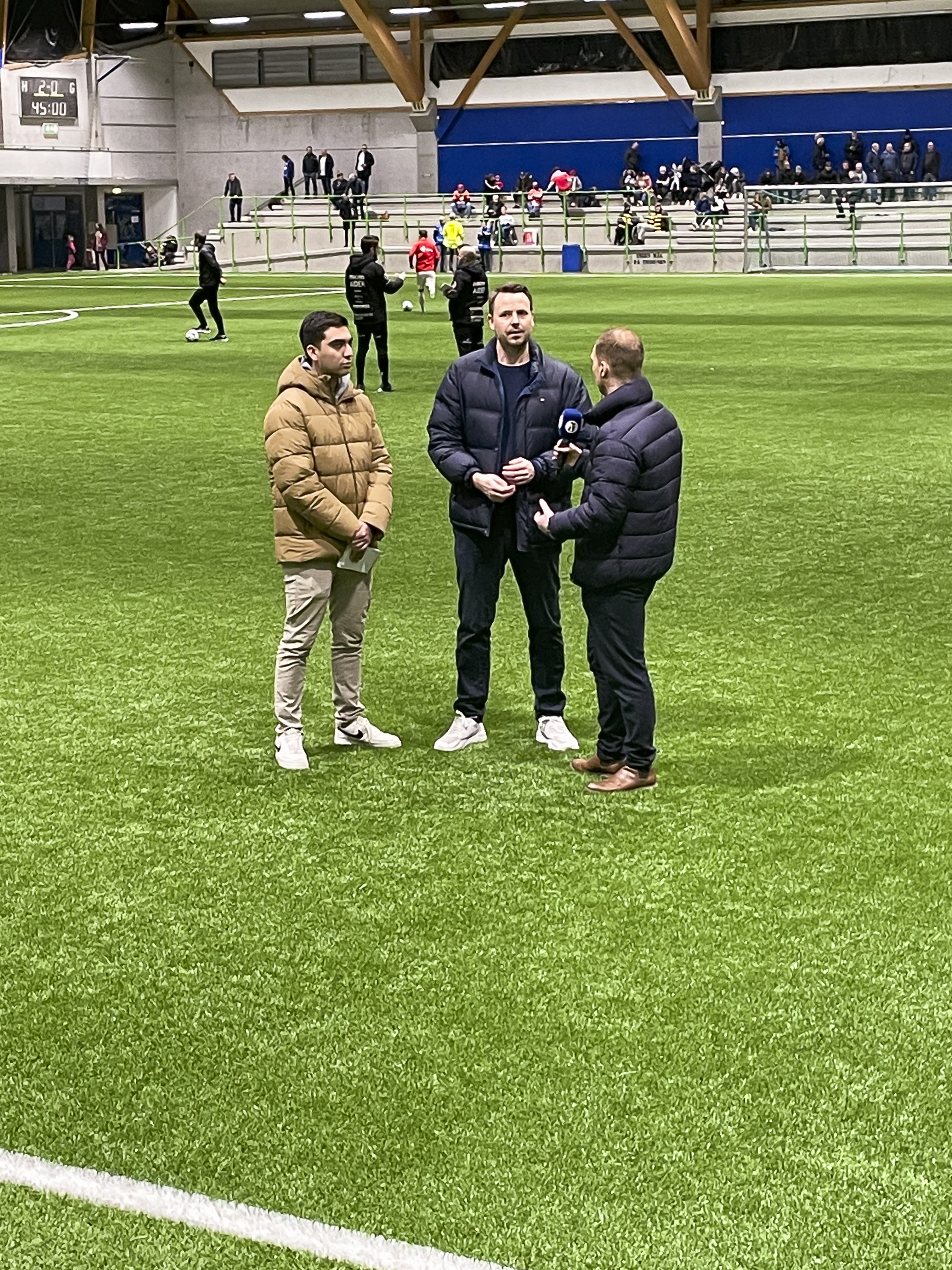 Tre menn står ute på fotballbanen og snakker sammen