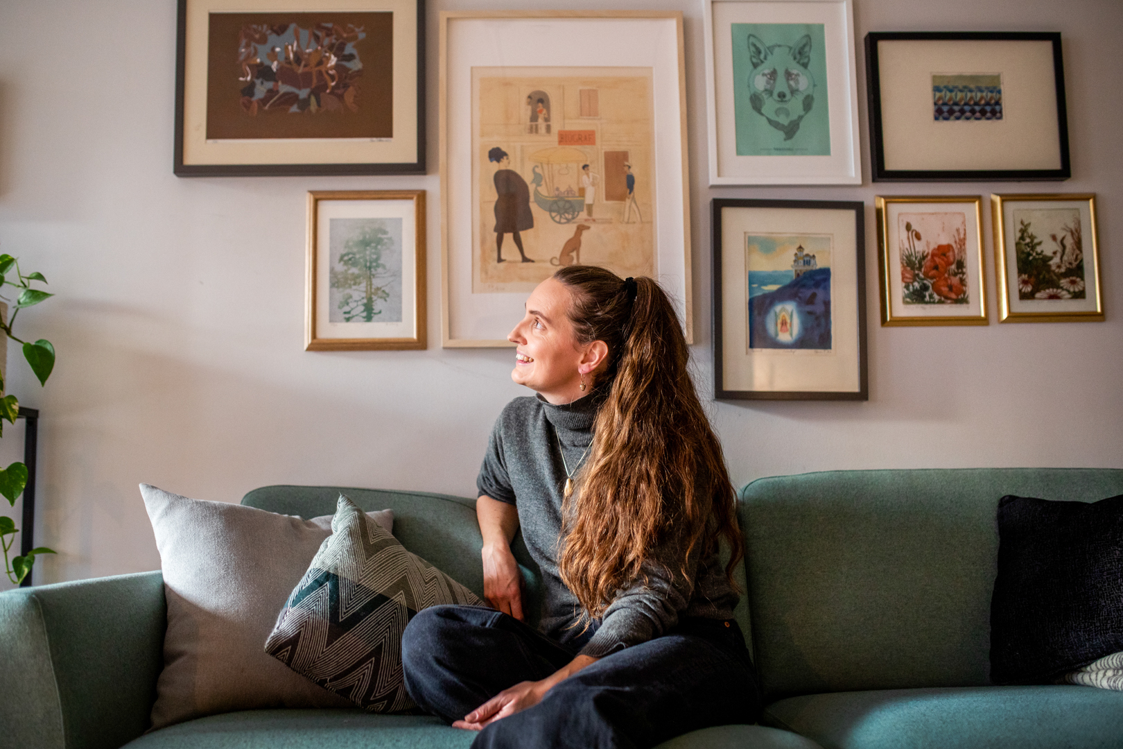 Birgitte sitter hjemme i sin grønne sofa. Veggen er full av fine bilder i ramme