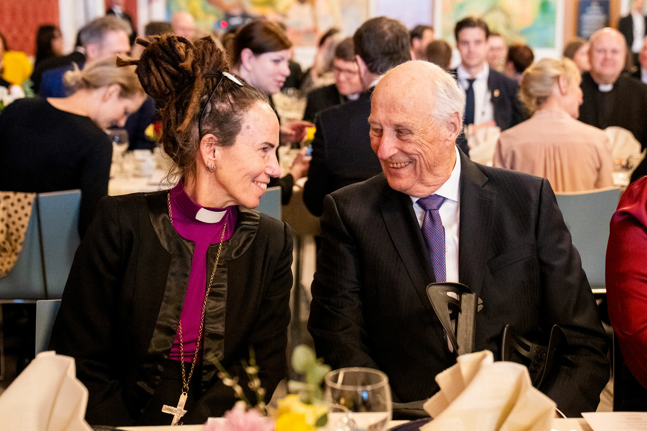 Foto: Biskopen sitter til bords sammen med konge. De ser på hverandre og smiler.