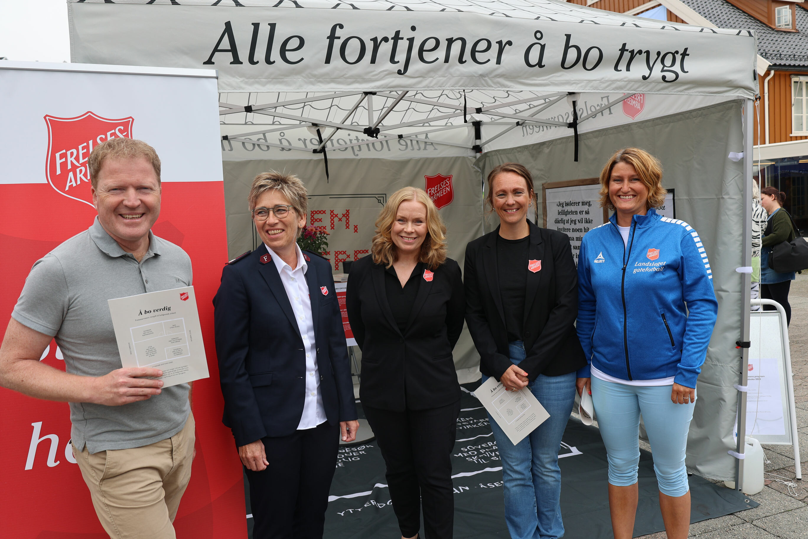 Fem personer på rekke, en mann og fire kvinner. Han holder opp en fersk boligrapport.