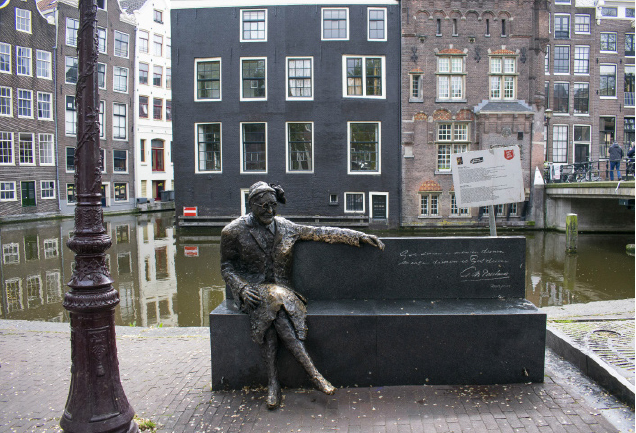 Bronseskulptur, plassert midt i en gate, som forstiller en kvinne i uniform på en benk. En husrekke står rett ved kanalen.
