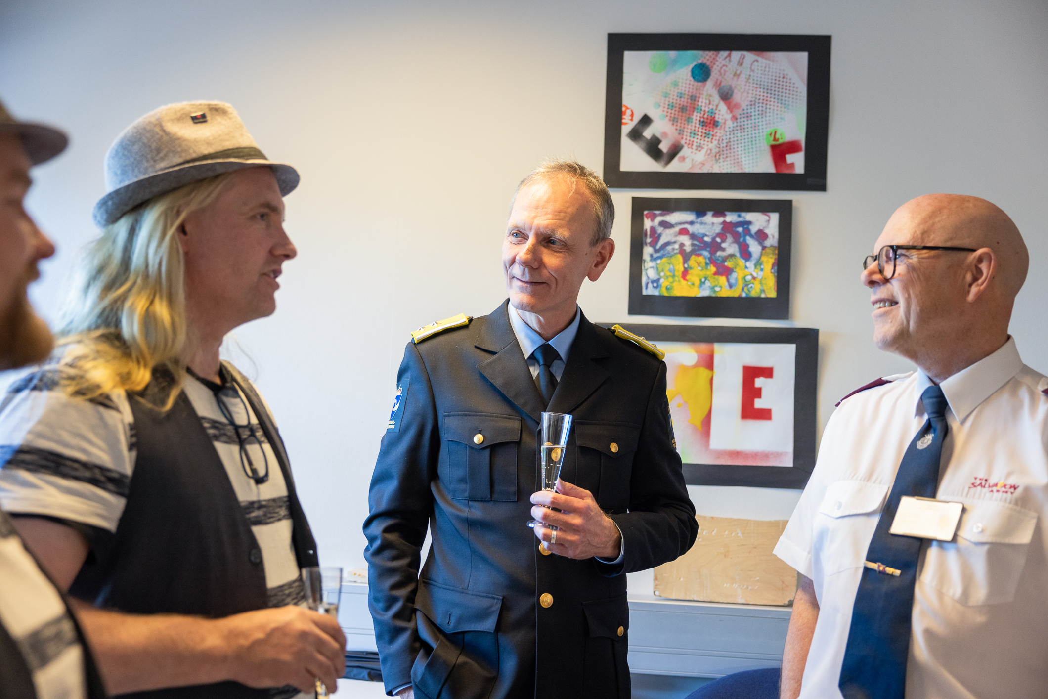 Tre menn prater sammen. Den ene har hvit og blå-stripete genser og vest med tørkle i halsen og en sixpence på hodet. Han i midten er tynn i håret og har fengselsomsorgens uniform og mannen til venstre er skallet, har briller og har Frelsesarmeens hvite uniformsskjorte og mørk bukse