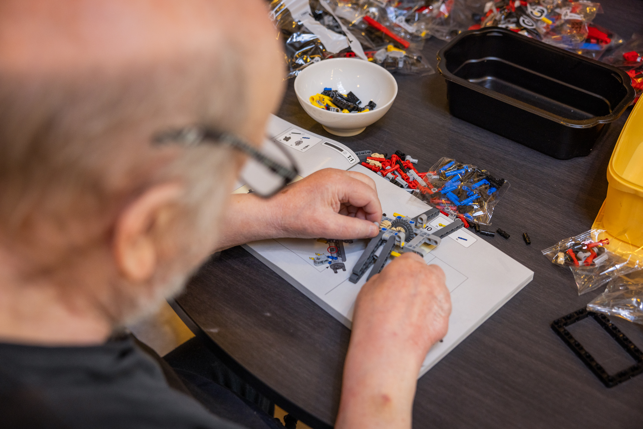 Mann sitter ved et bord og pusler med små brikker i klare farger – gule, blå og røde plastbrikker.