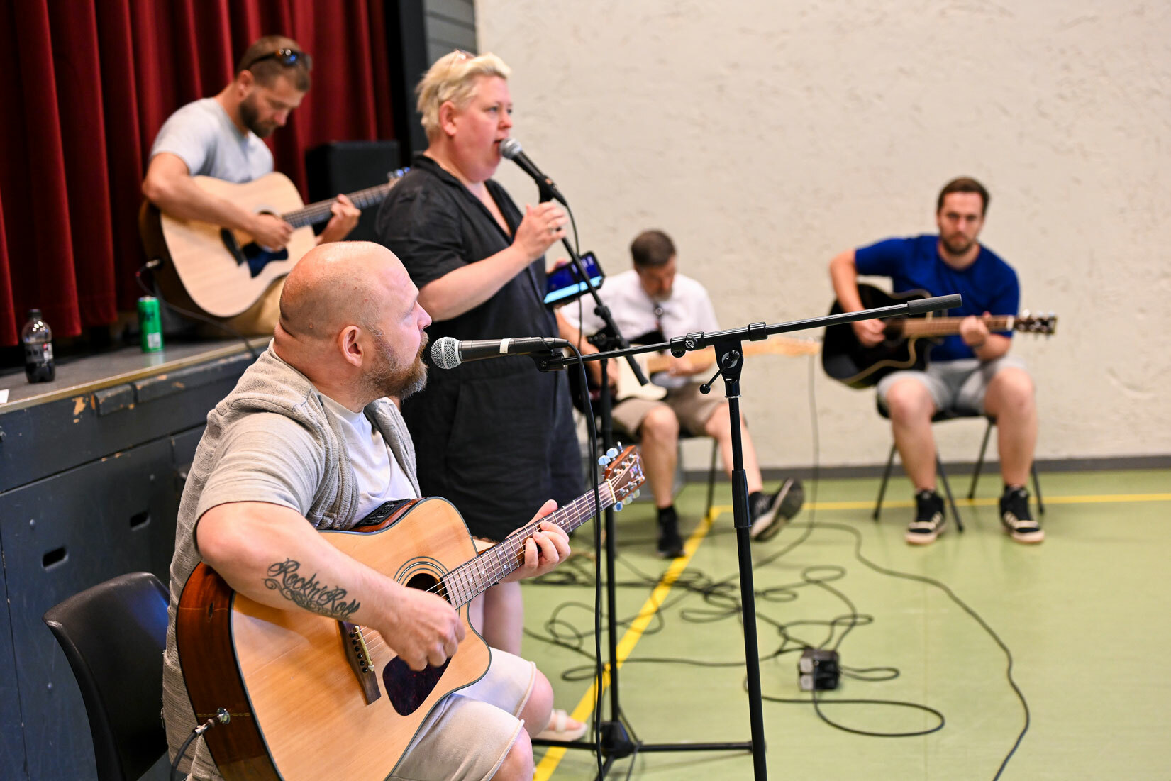Band som øver. Fire menn på gitar, en av mennene og en kvinne synger.