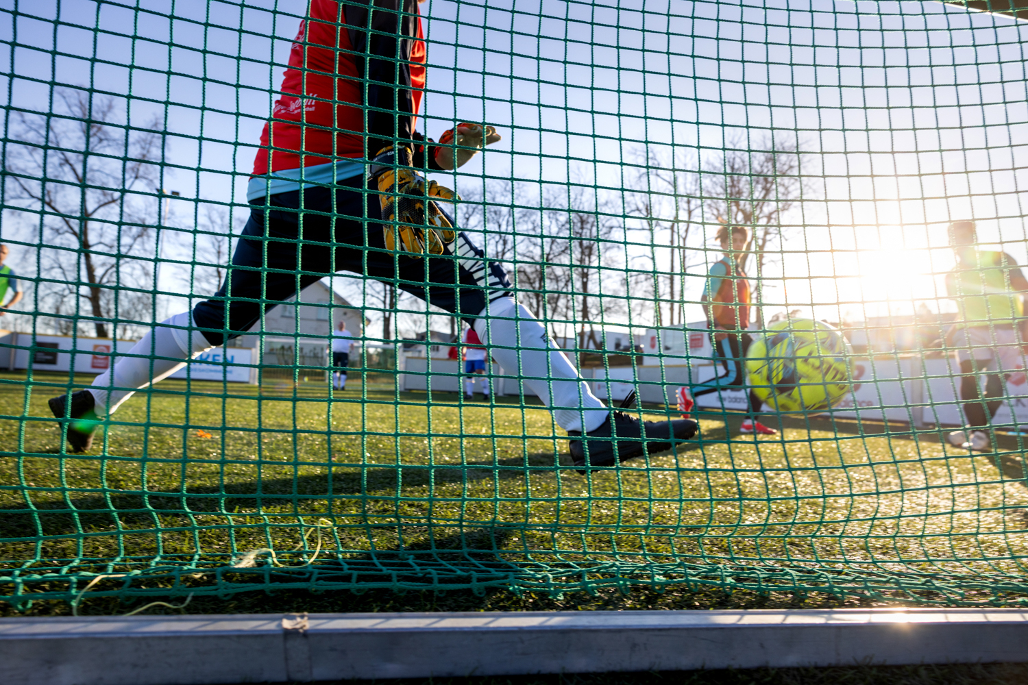 Foto: Flere fotballspillere sees gjennom nettingen på det lille målet. Banen er også liten.