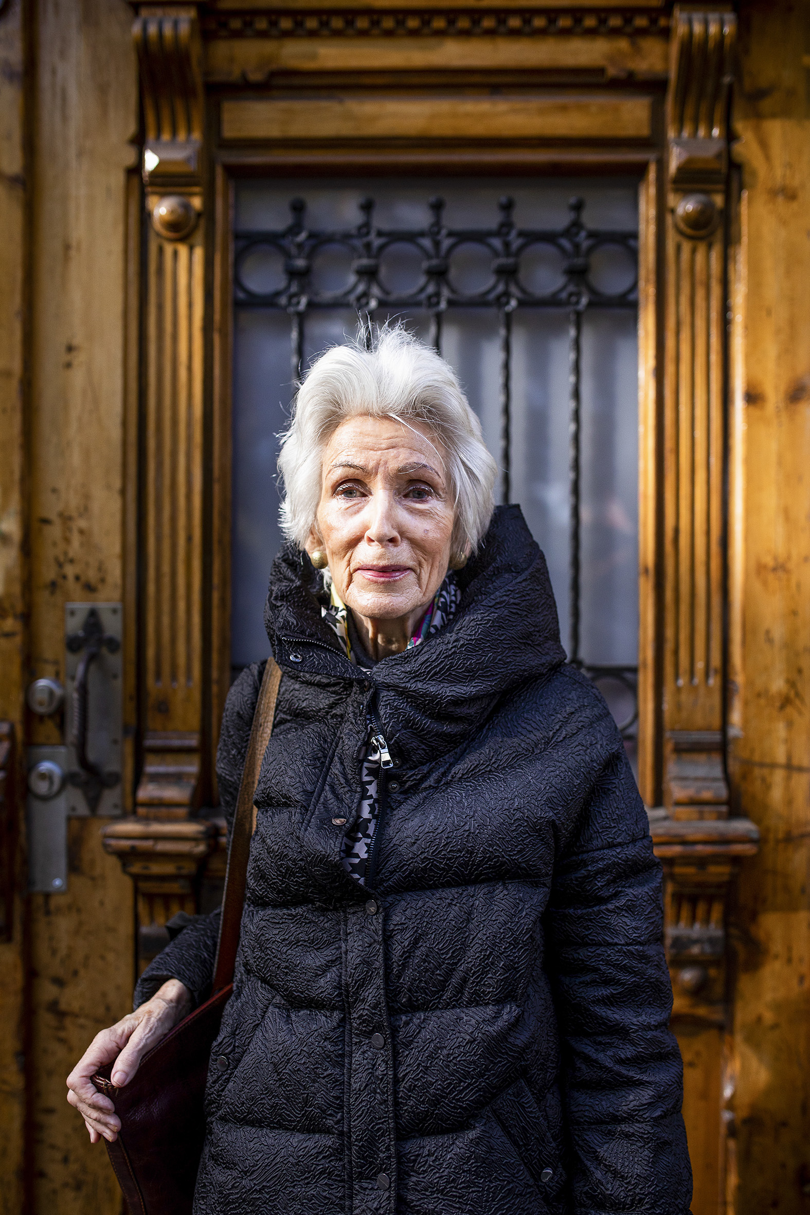 Charlotte foran en gammel tredør iført en pen dunjakke og med veska på skulderen.
