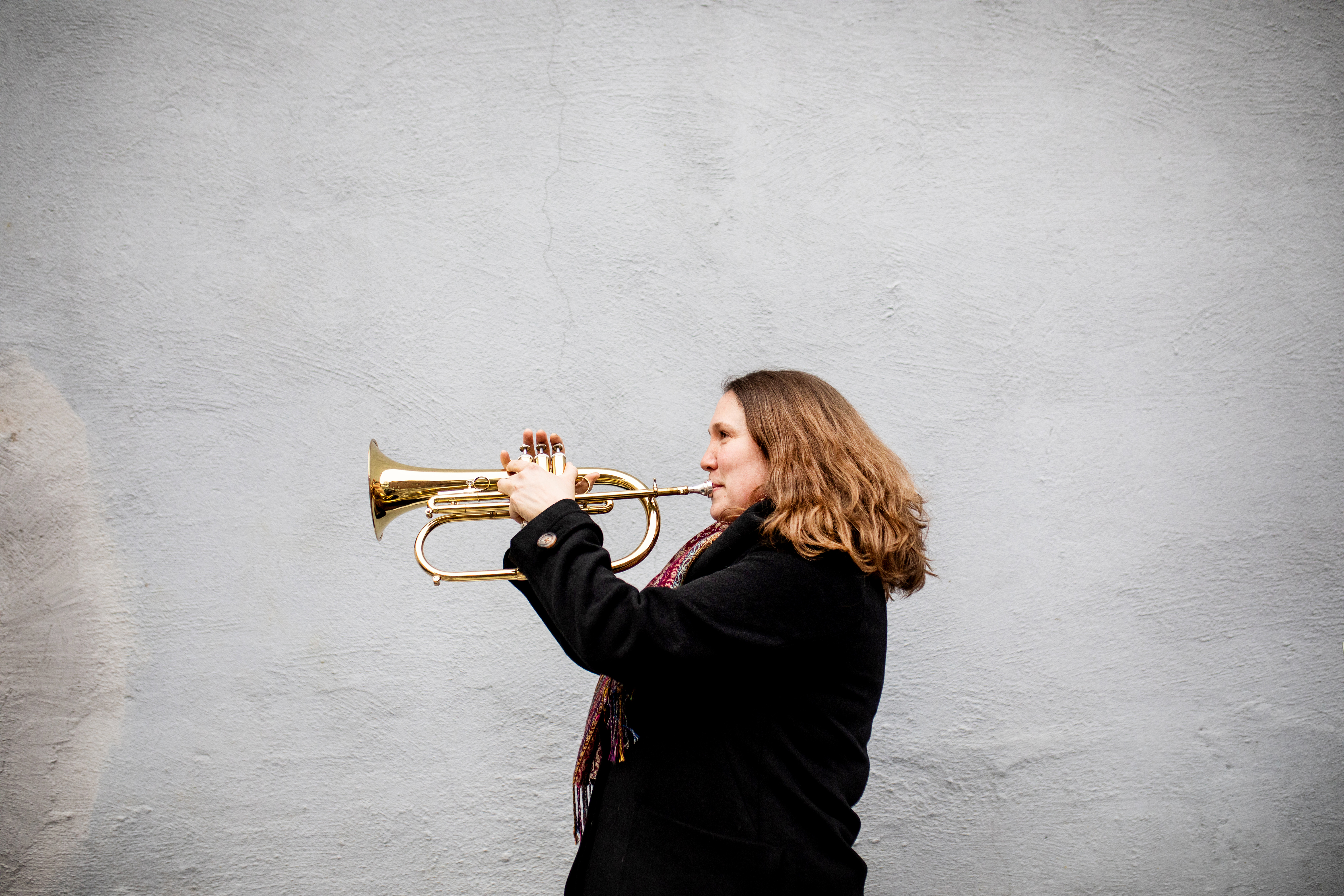 Christine spiller på hornet sitt foran en grå murvegg.