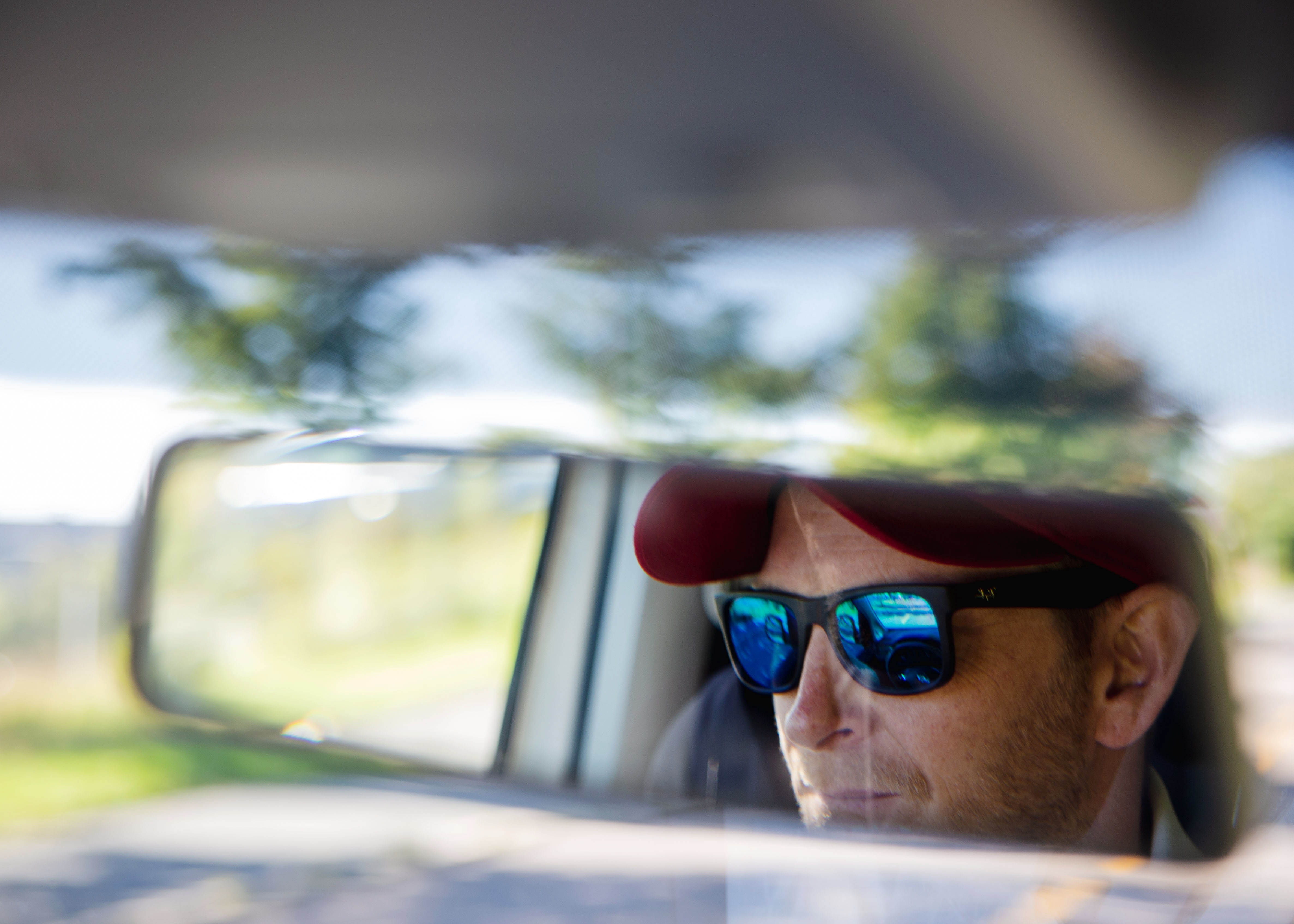 Ansiktet på sjåfør med solbriller i bakspeilet i bil