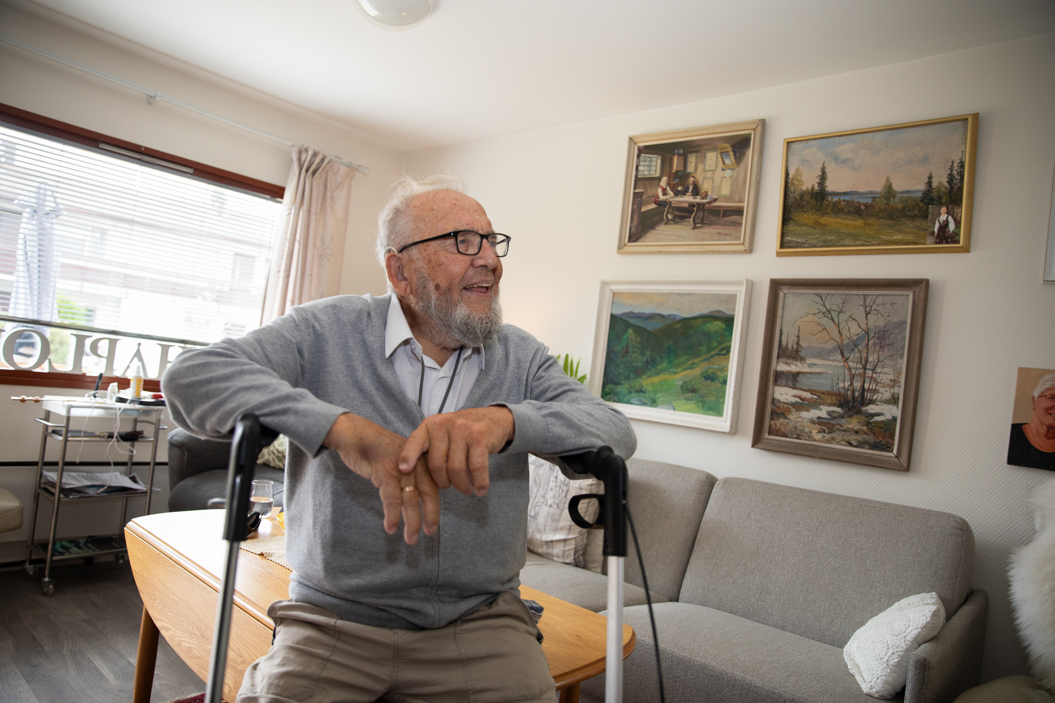 Gammel mann som hviler seg på en rullator i stua.