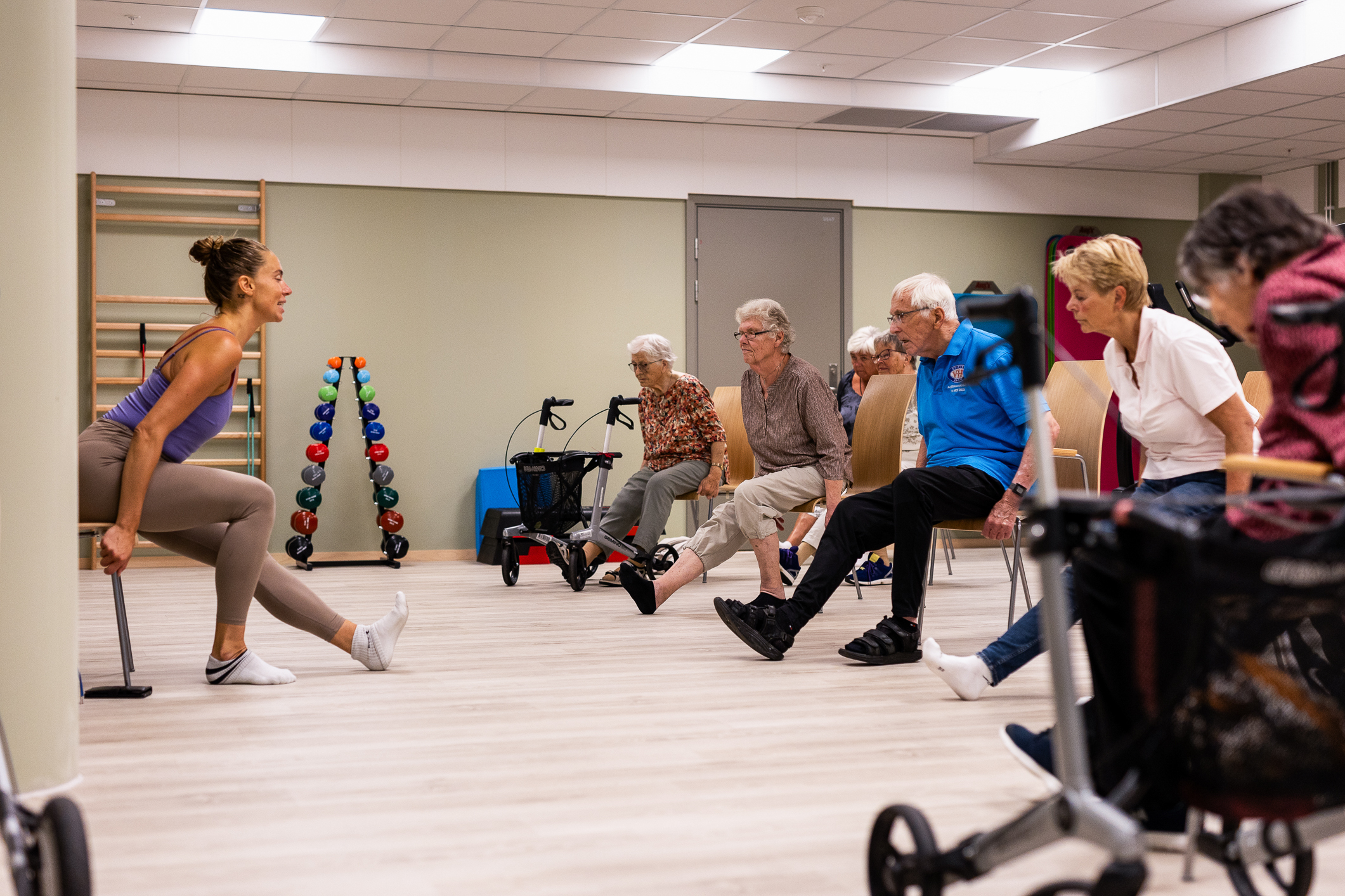 Instruktør som viser stolrekker med eldre hvordan de tøyer ut føttene.