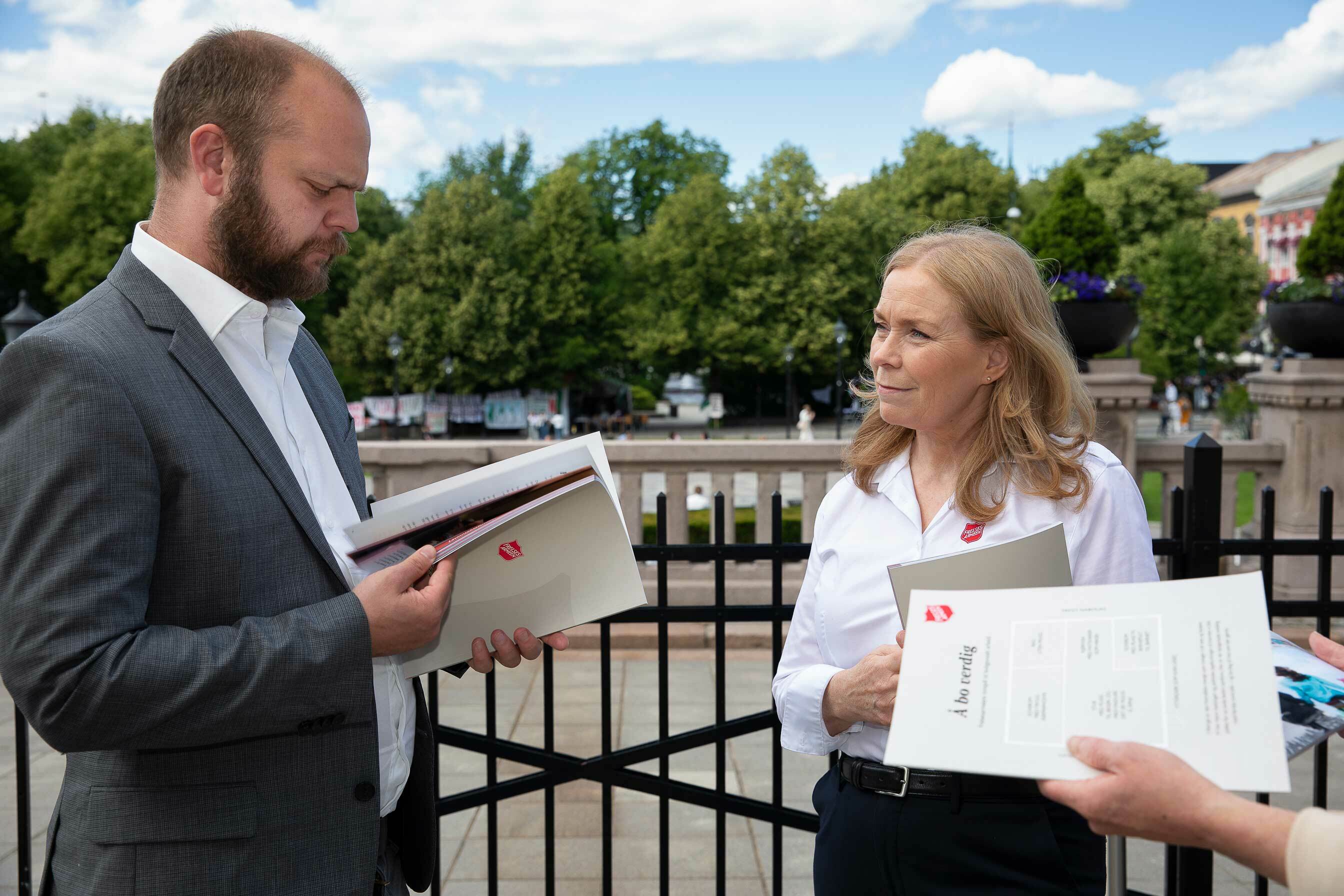 En mann med dress og skjorte leser en rapport han har fått av en kvinne fra Frelsesarmeen.