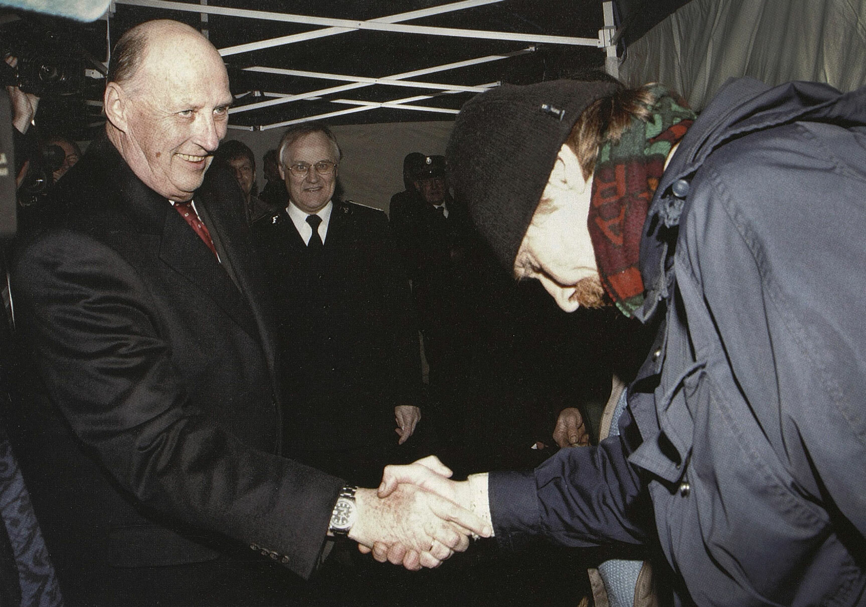 Foto: En mann med lue og skjerf bukker dypt når han hilser på en eldre mann i svart jakke og slips inne i et telt.