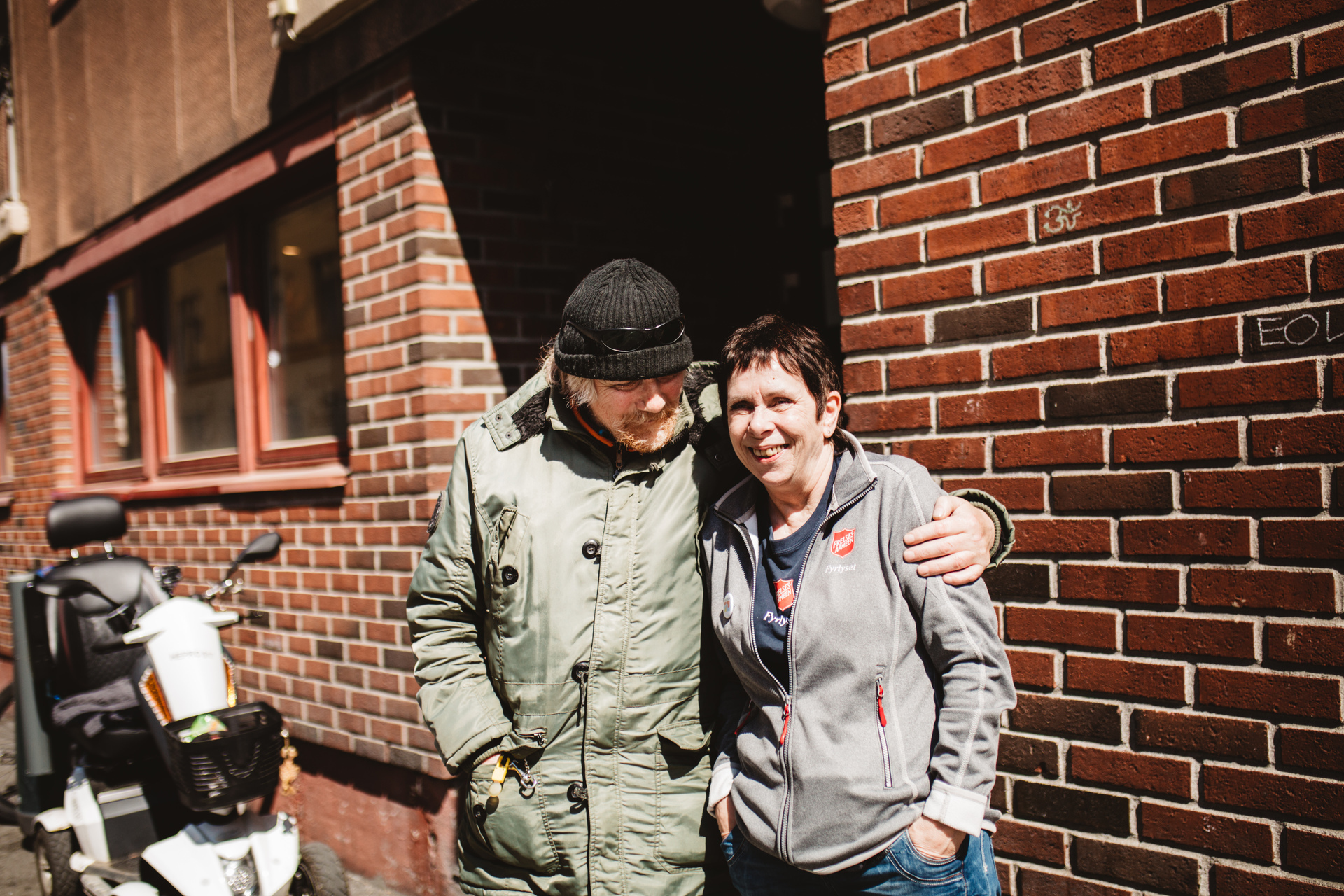 Foto: Eldre mann i grønn parkas holder rundt en dame tidlig i 60-årene med mørkt hår.