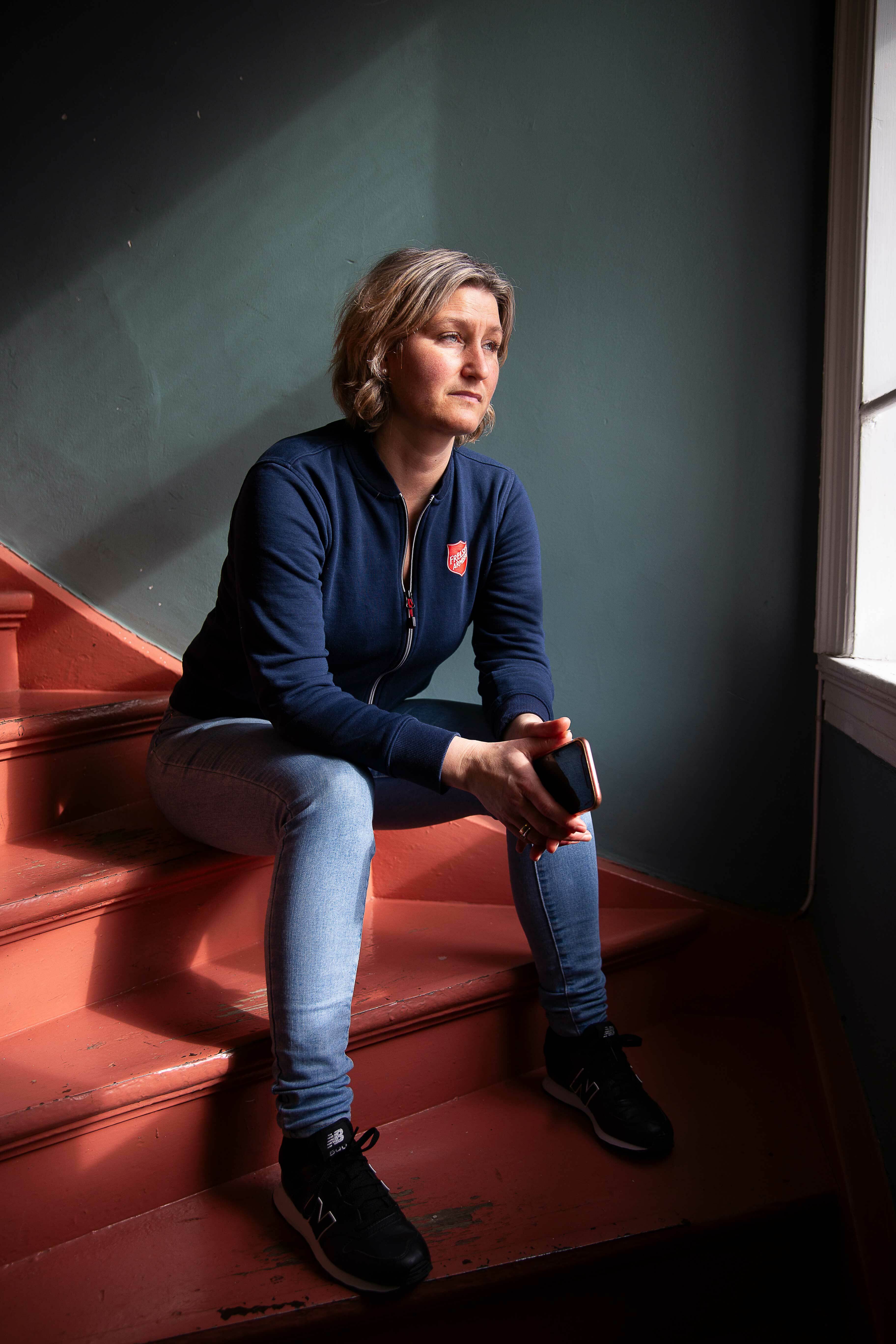 Foto: En kvinne i blå jakke og olabukser sitter i en rødmalt trapp