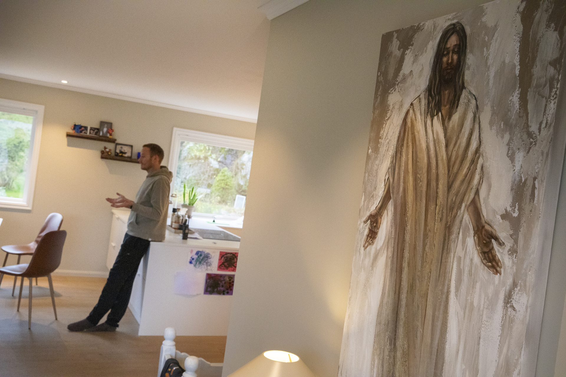 En mann lener seg til en kjøkkenøy i et lyst rom. Et maleri av Jesus i forgrunnen.