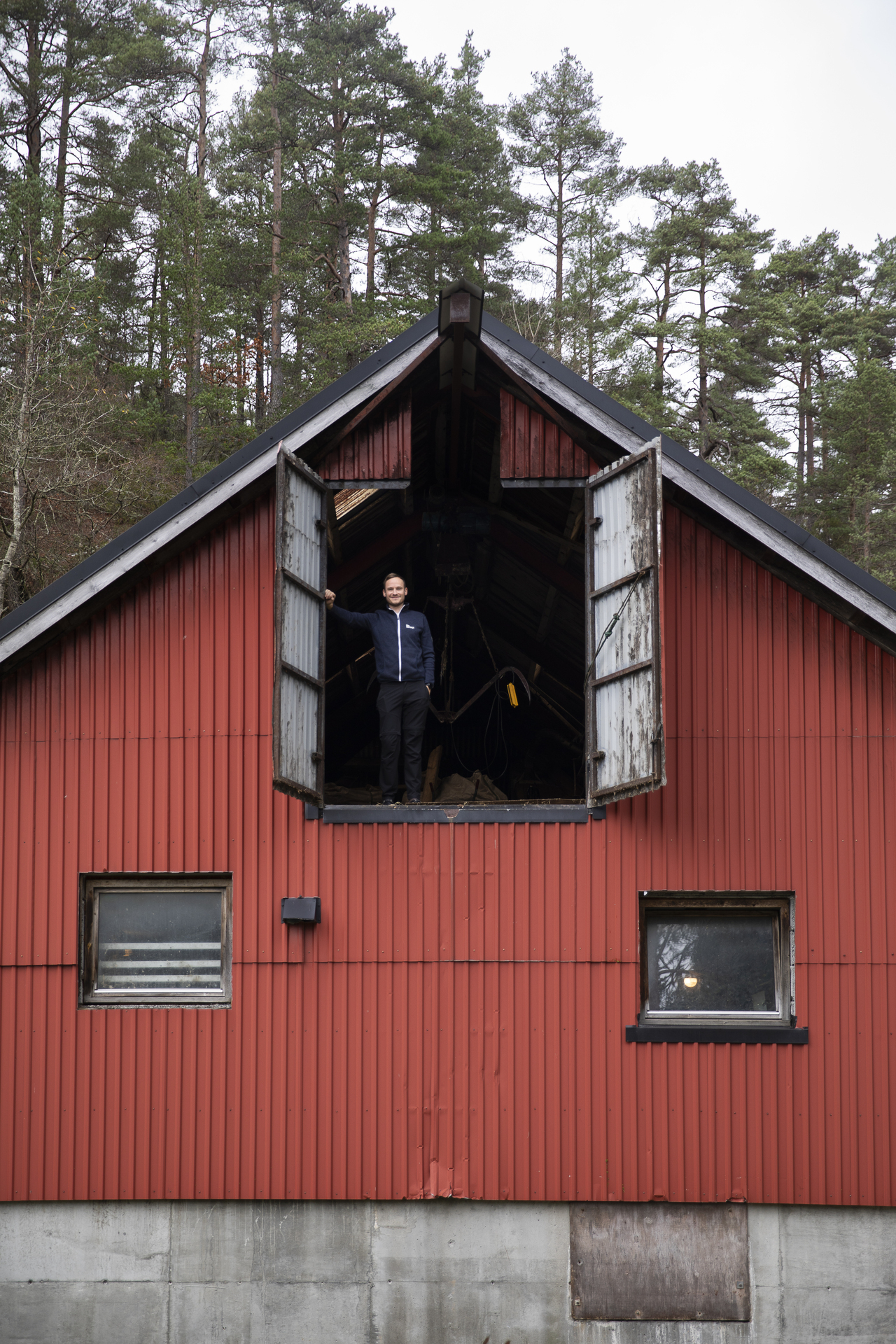 En mann står oppe på låven i en dørluke oppe på  den røde låveveggen